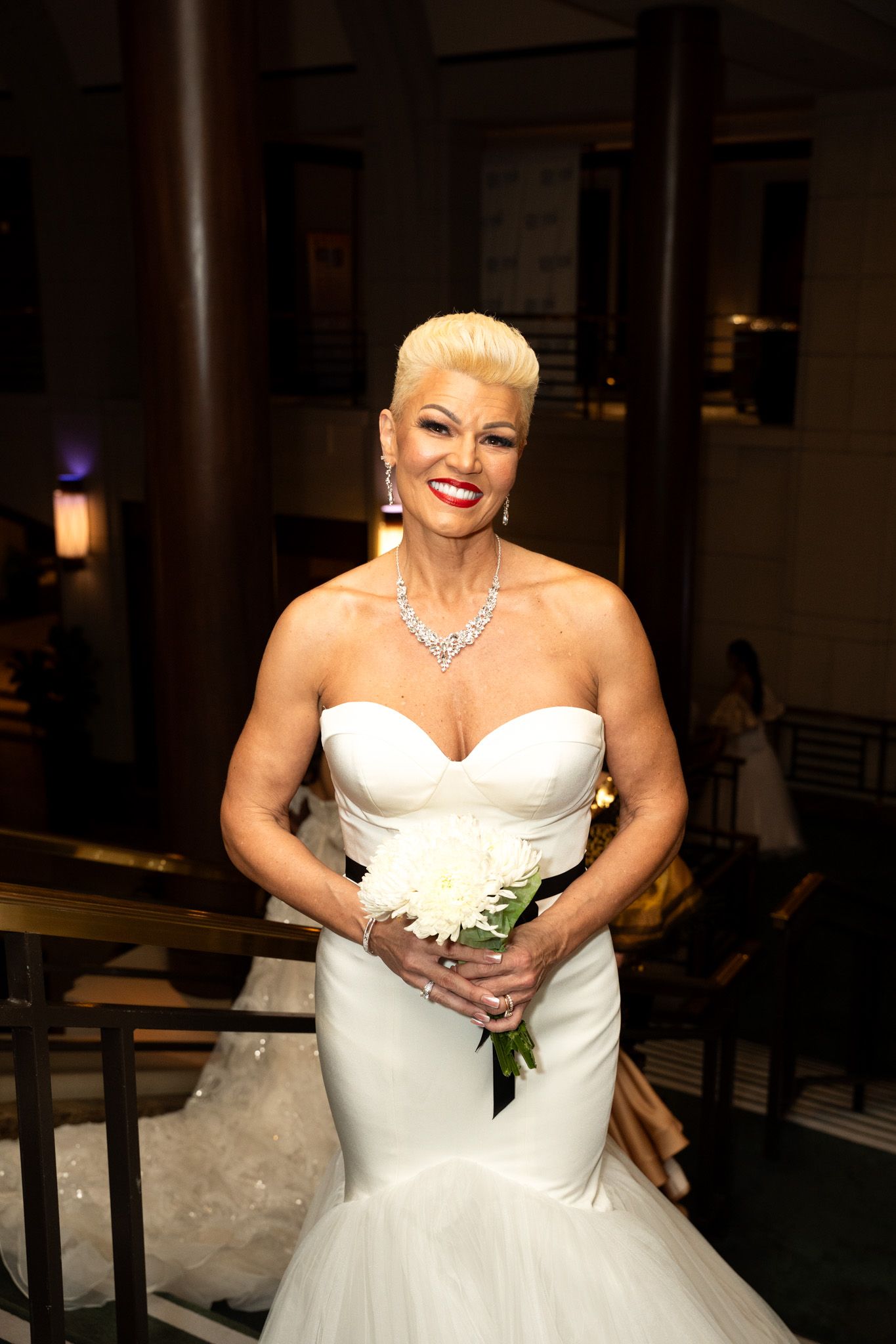A bride in a strapless white wedding gown with a sweetheart neckline poses elegantly in an indoor setting.