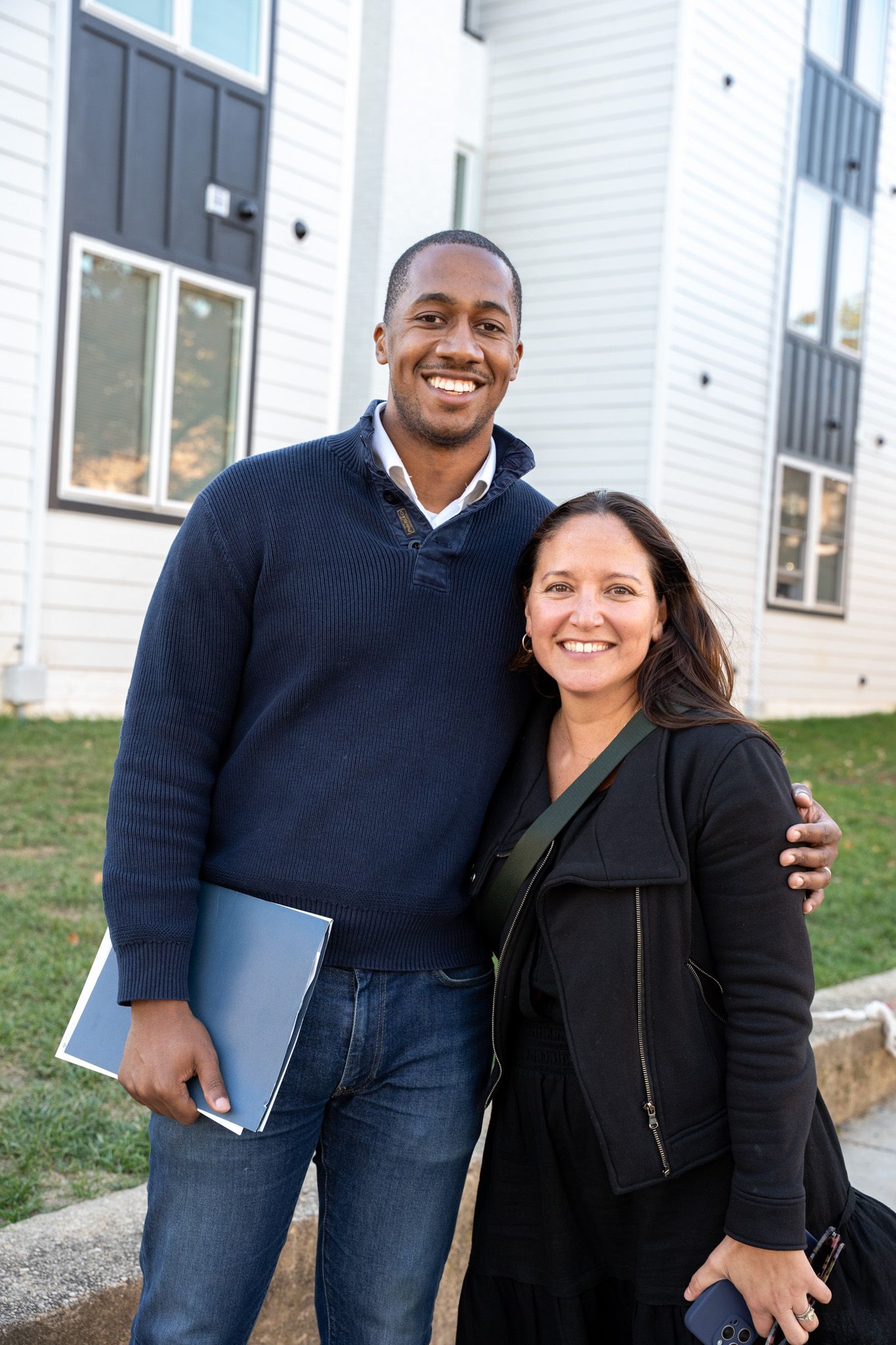 People smiling and posing together outside a white building on a sunny day.