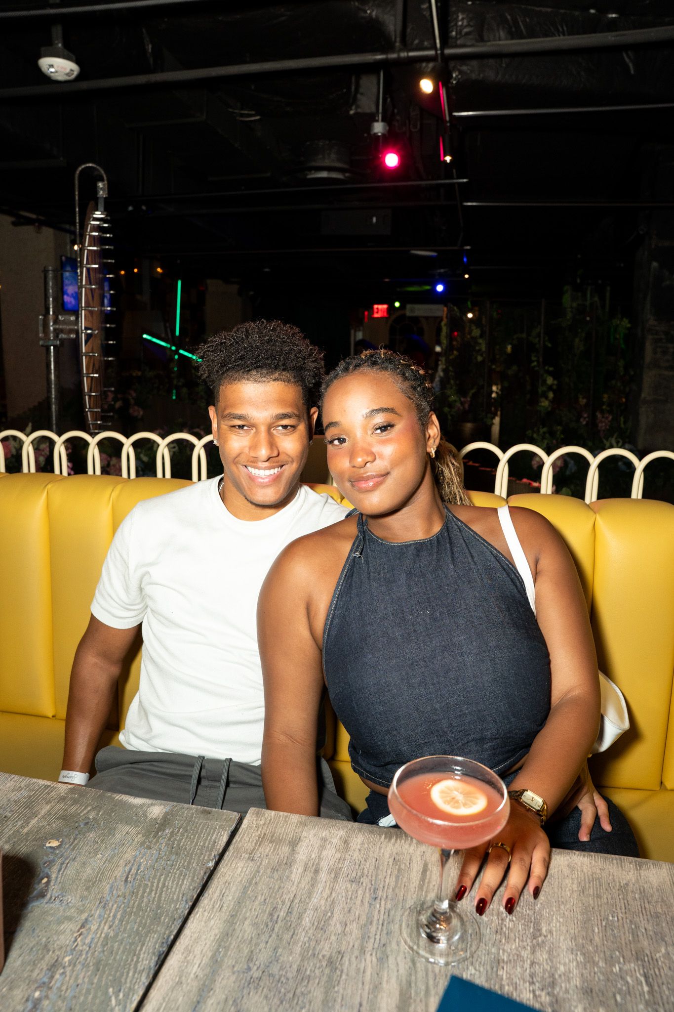 Friends sharing a cozy moment at a booth with yellow seating in a dimly lit venue.