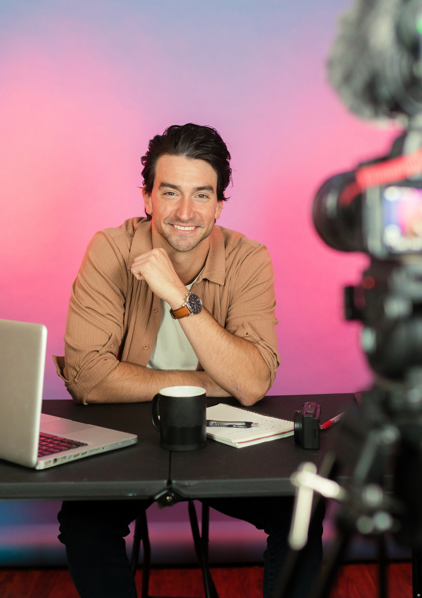 Content creator in casual attire posing during video production against pink backdrop.