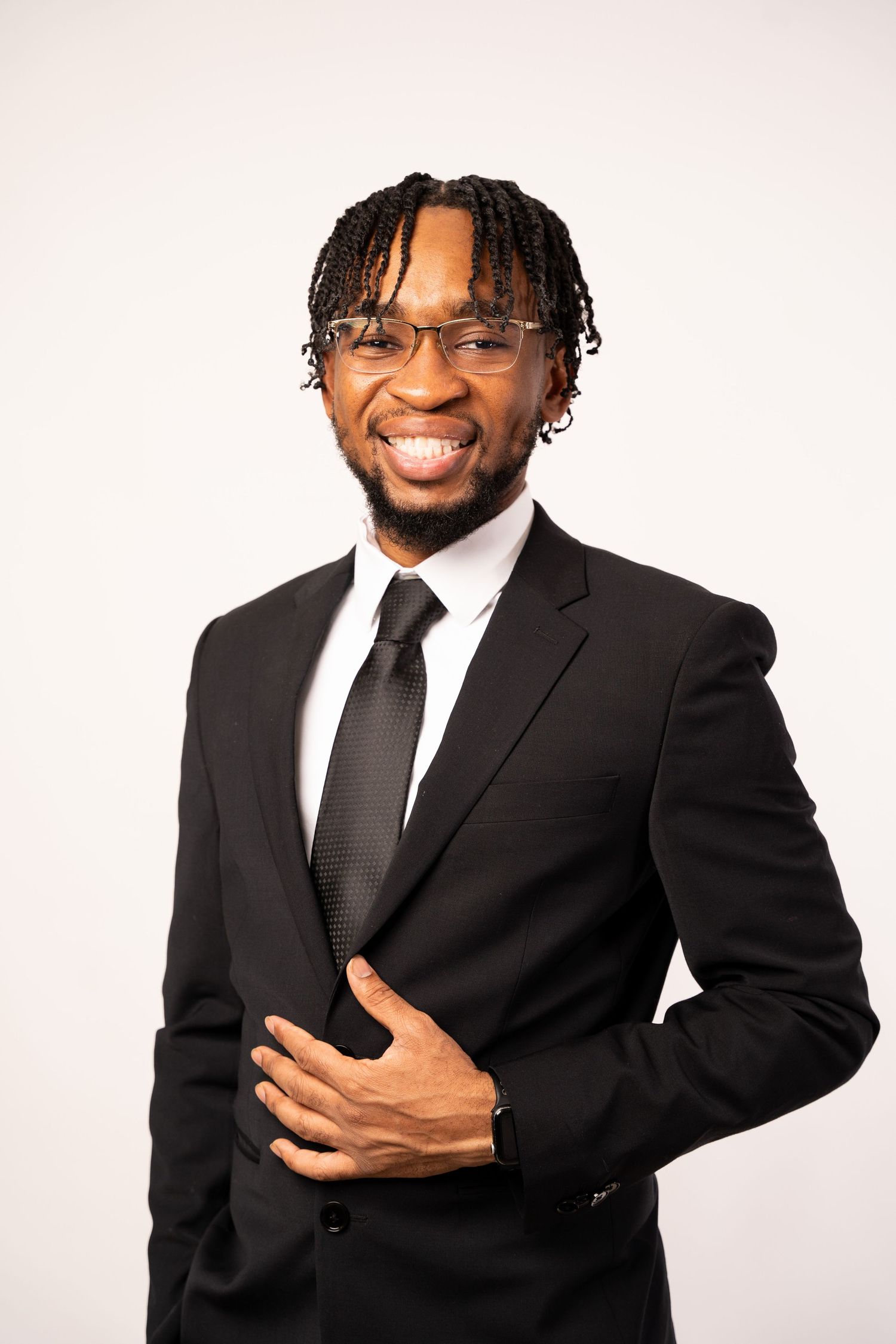 Professional portrait of someone in a black suit and tie posing against white background.