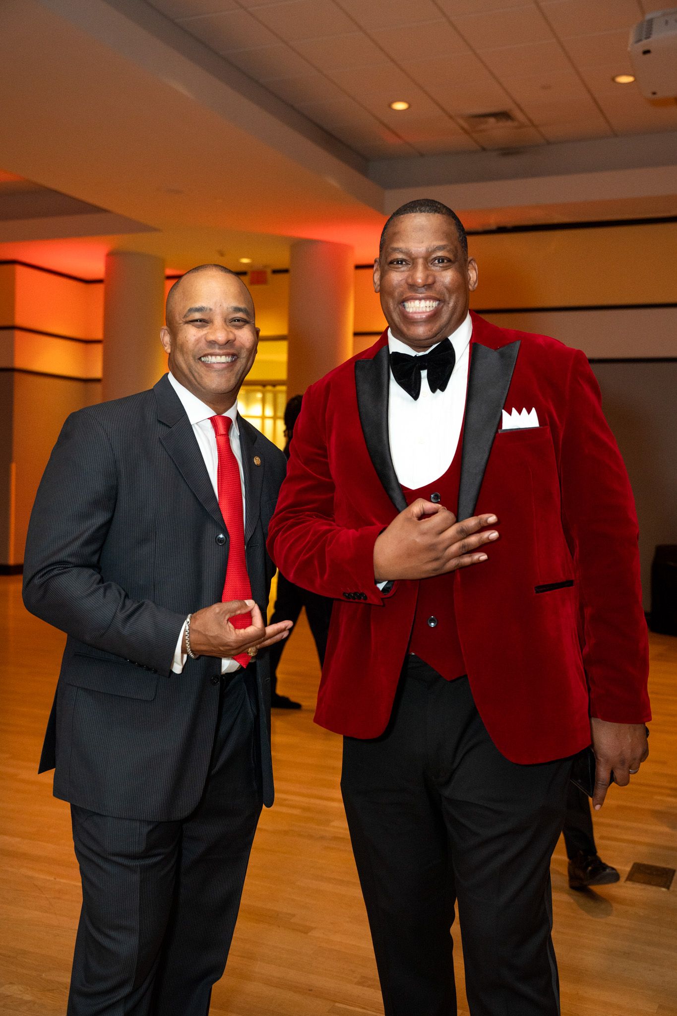 Two guests in formal attire at an elegant event, one wearing a striking red velvet jacket.