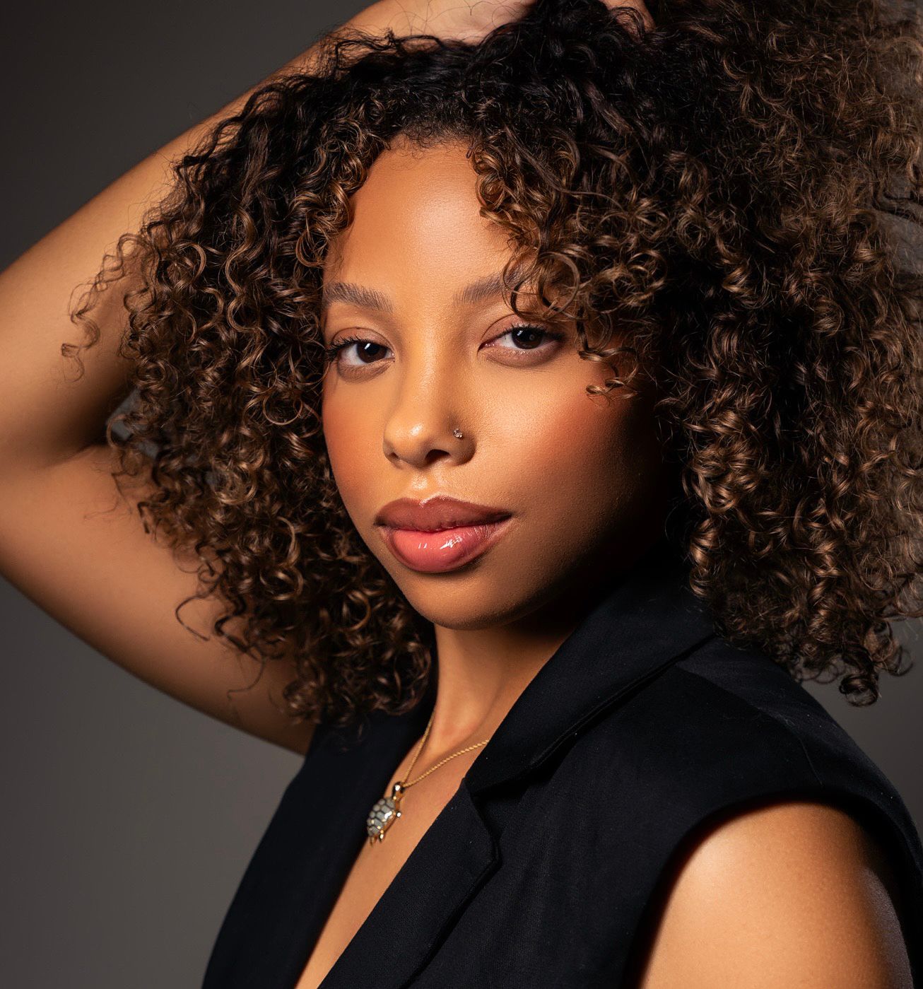 Artistic headshots with natural curly hair and black blazer against moody lighting.