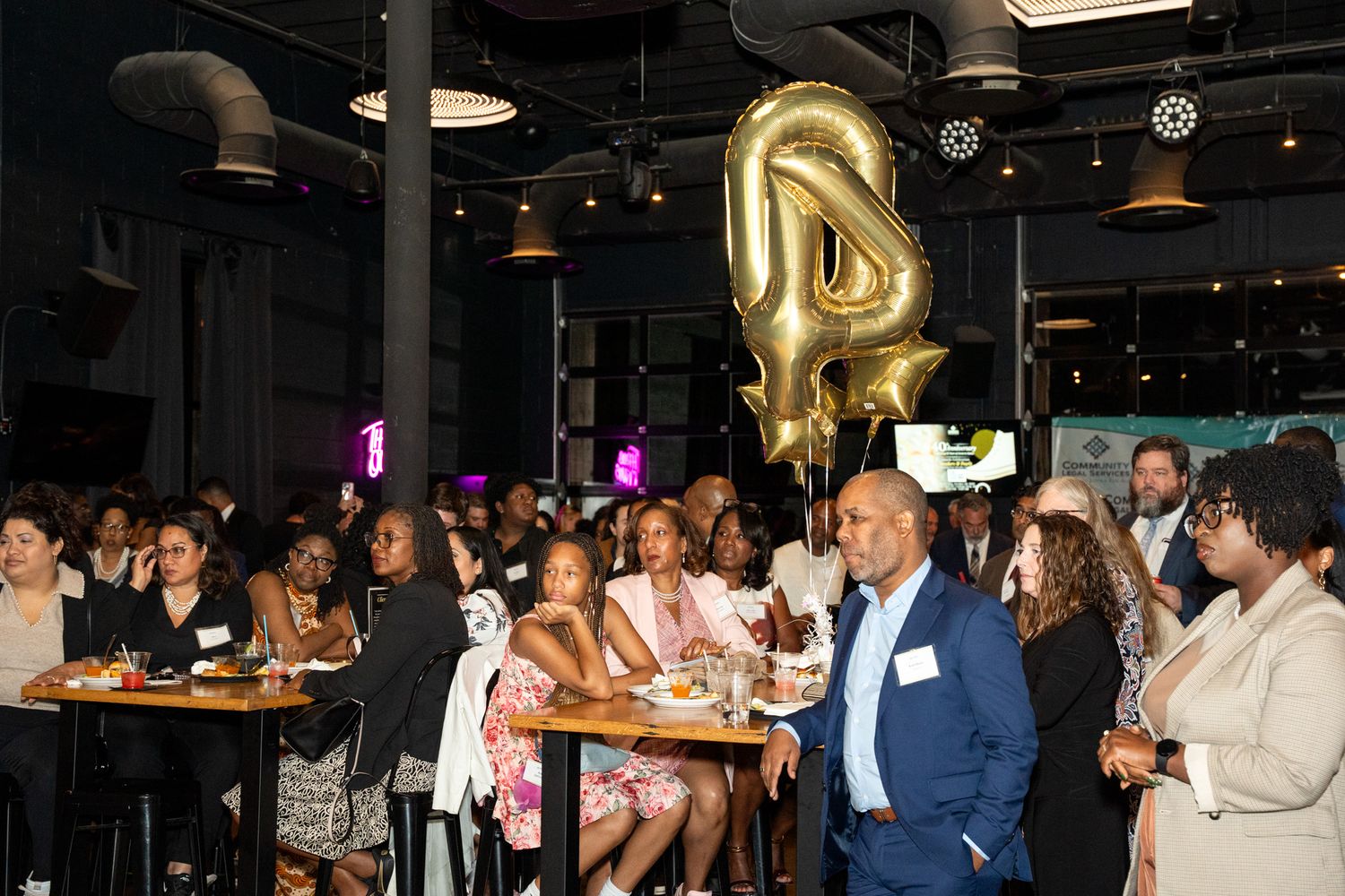 Crowded venue with gold balloon decorations during celebration event.