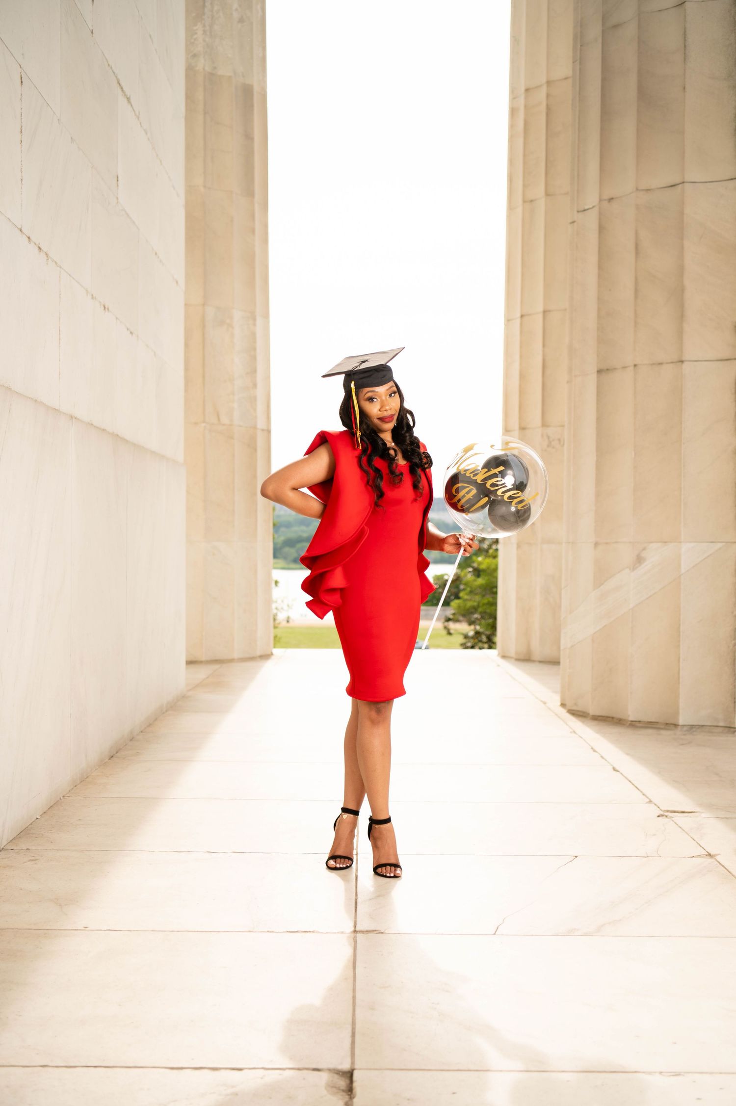 Graduate in fitted red dress poses elegantly between architectural columns.