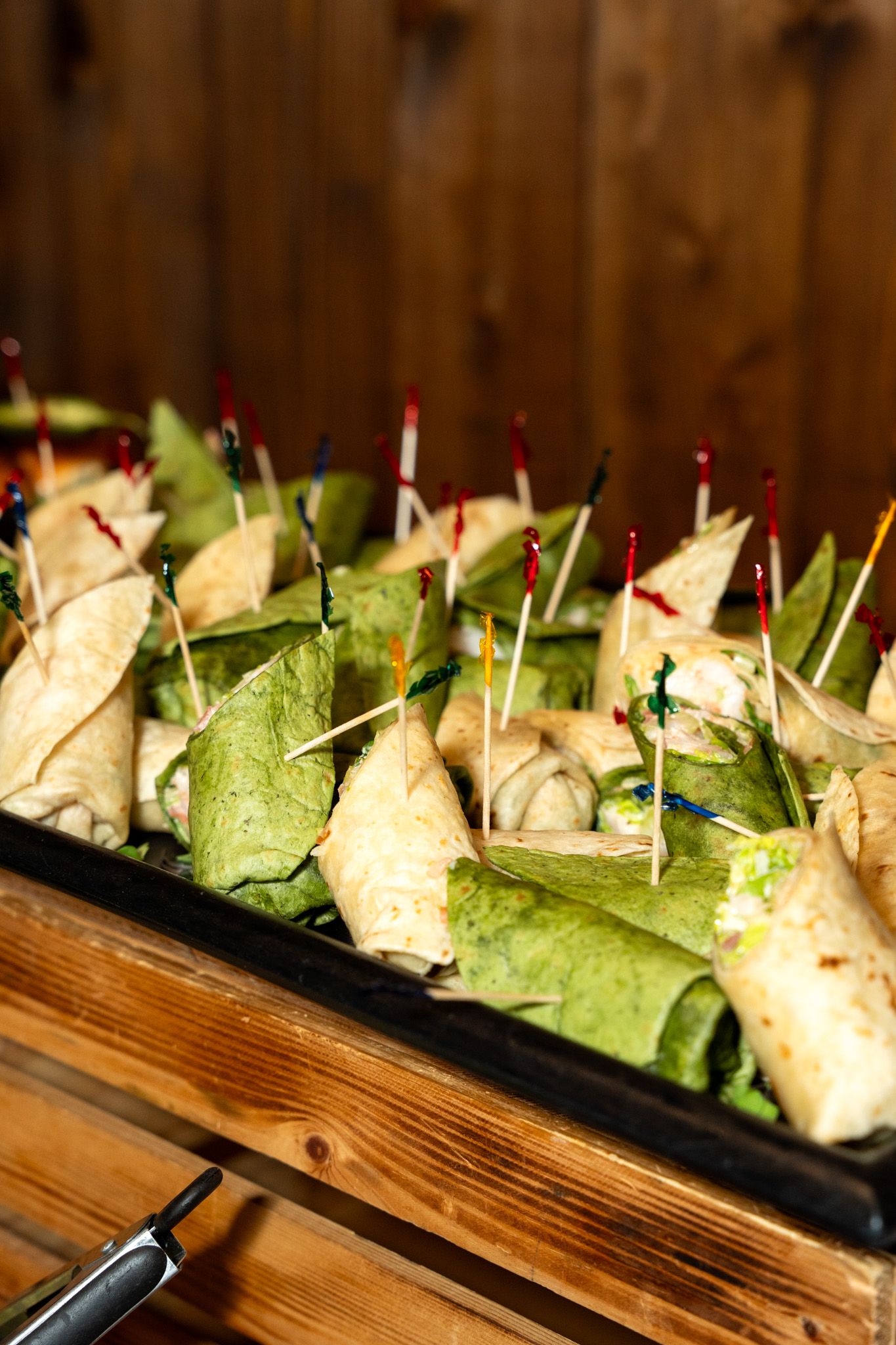 Catered sandwich bites with toothpicks arranged on a wooden serving board.