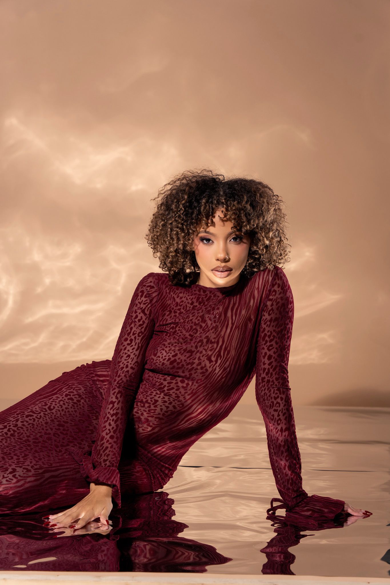 A model in a burgundy velvet dress poses dramatically against a sepia-toned background in a fashion editorial series.