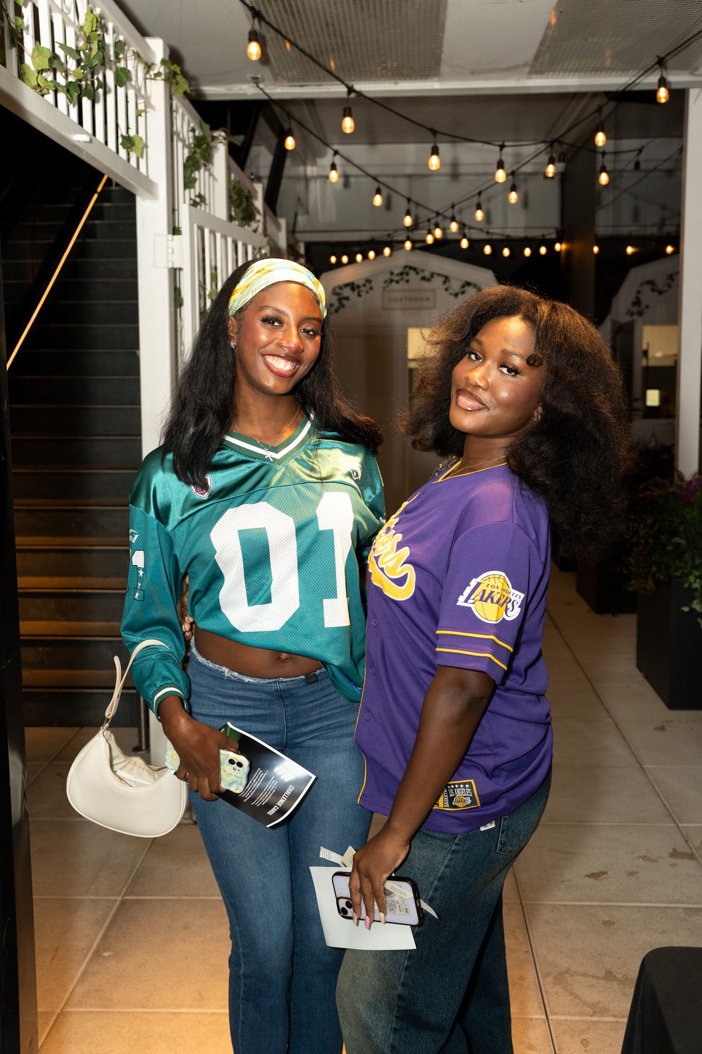Two people in sports jerseys posing together under string lights.