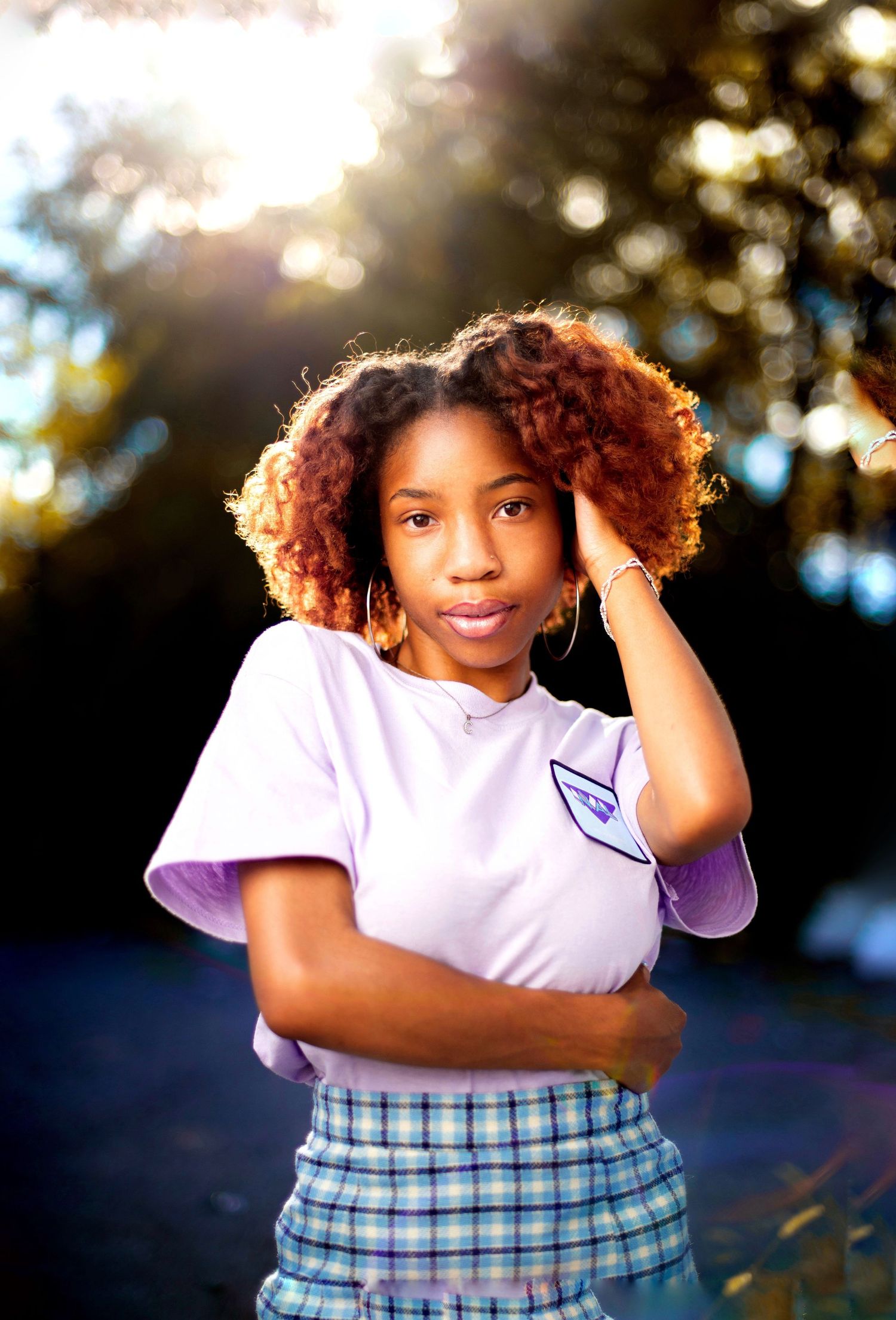 Portrait of person in white t-shirt and plaid skirt with curly hair at sunset.