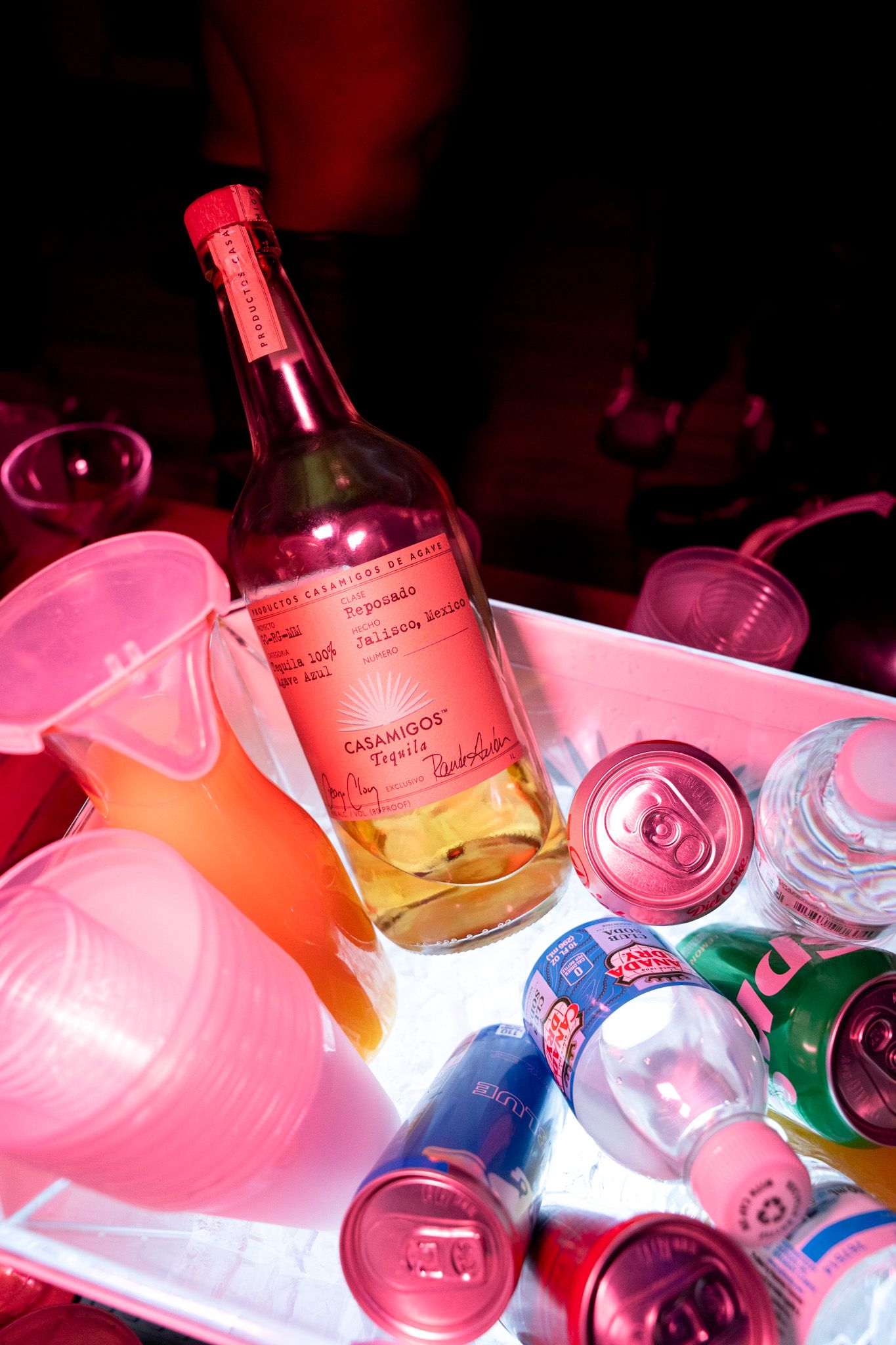 A bottle of wine and various drinks chill in a pink-lit ice bucket.