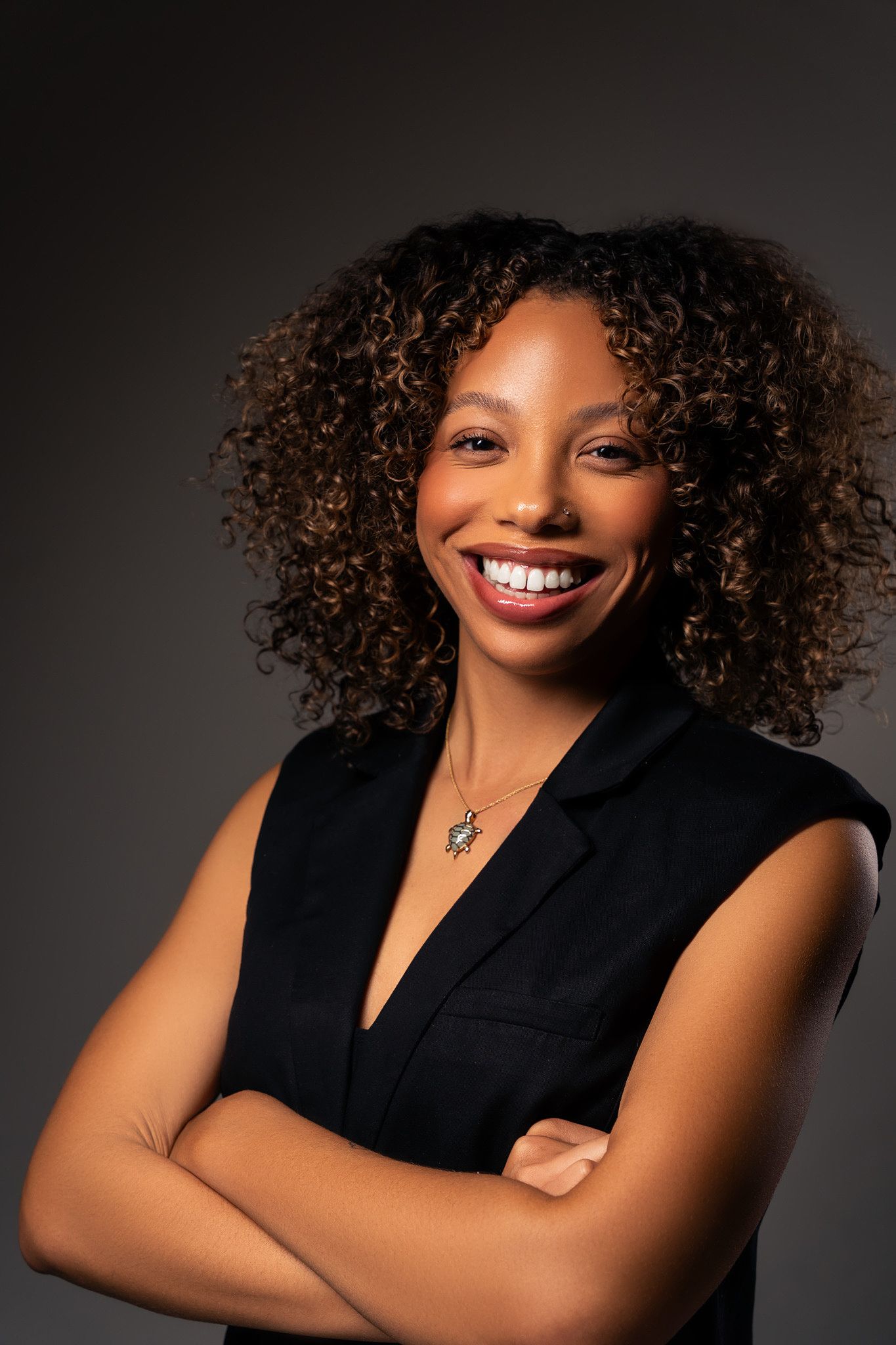 Confident poses in black sleeveless blazer with natural curly hair in professional studio setting.