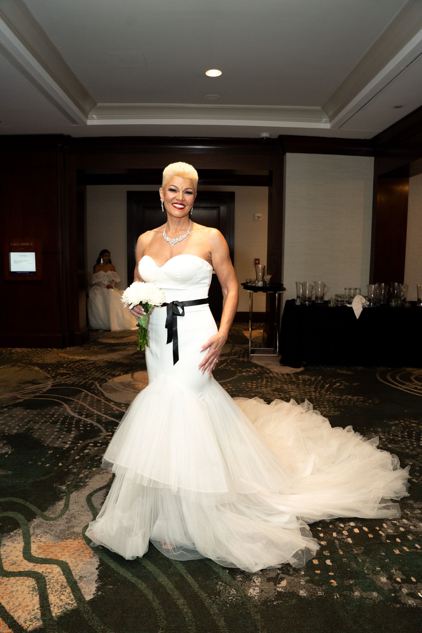 Model showcases white tulle ballgown with black sash on fashion runway.