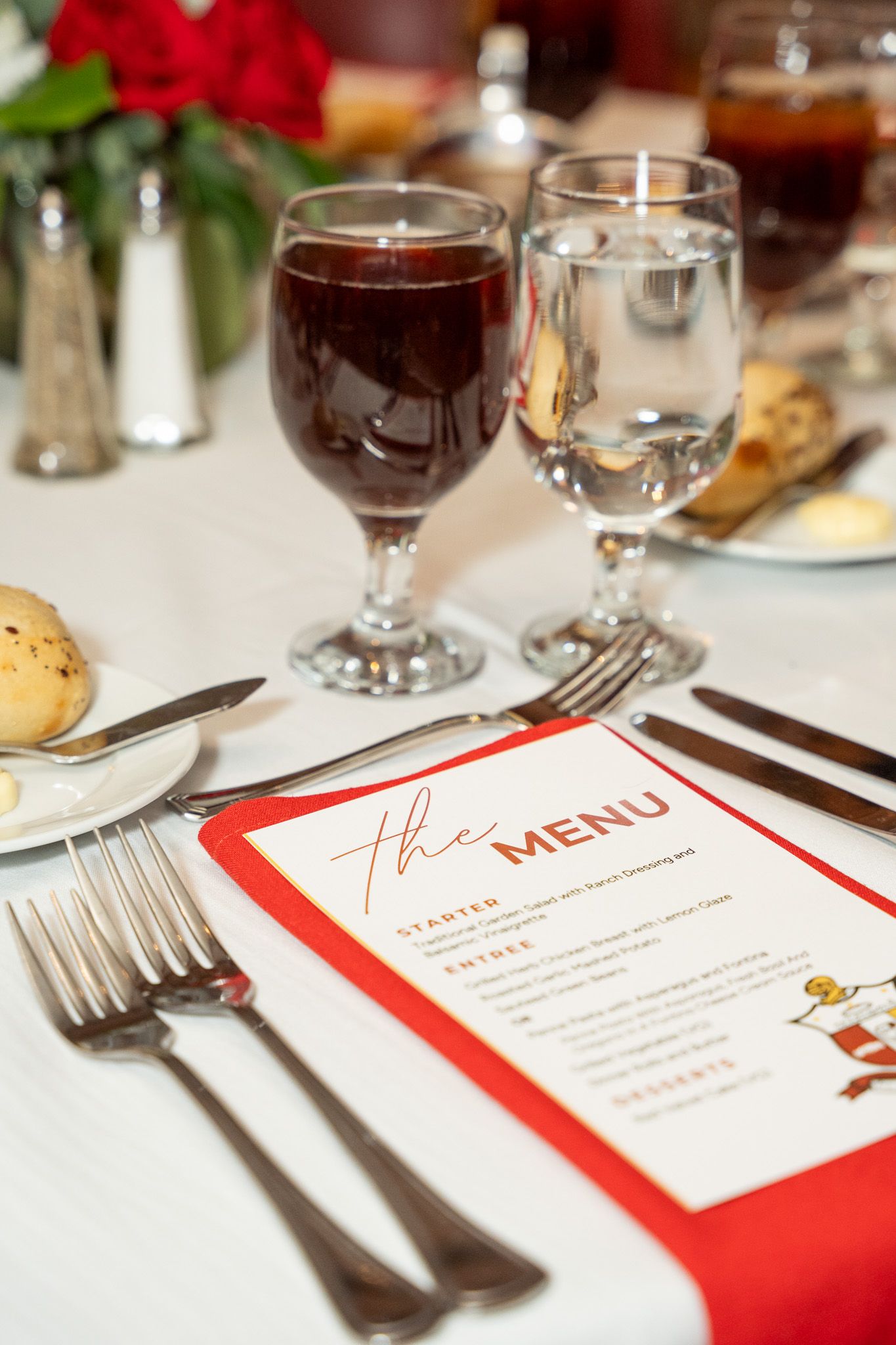 Elegant place setting with wine glasses, menu card with red border, and table settings at a formal dinner event.