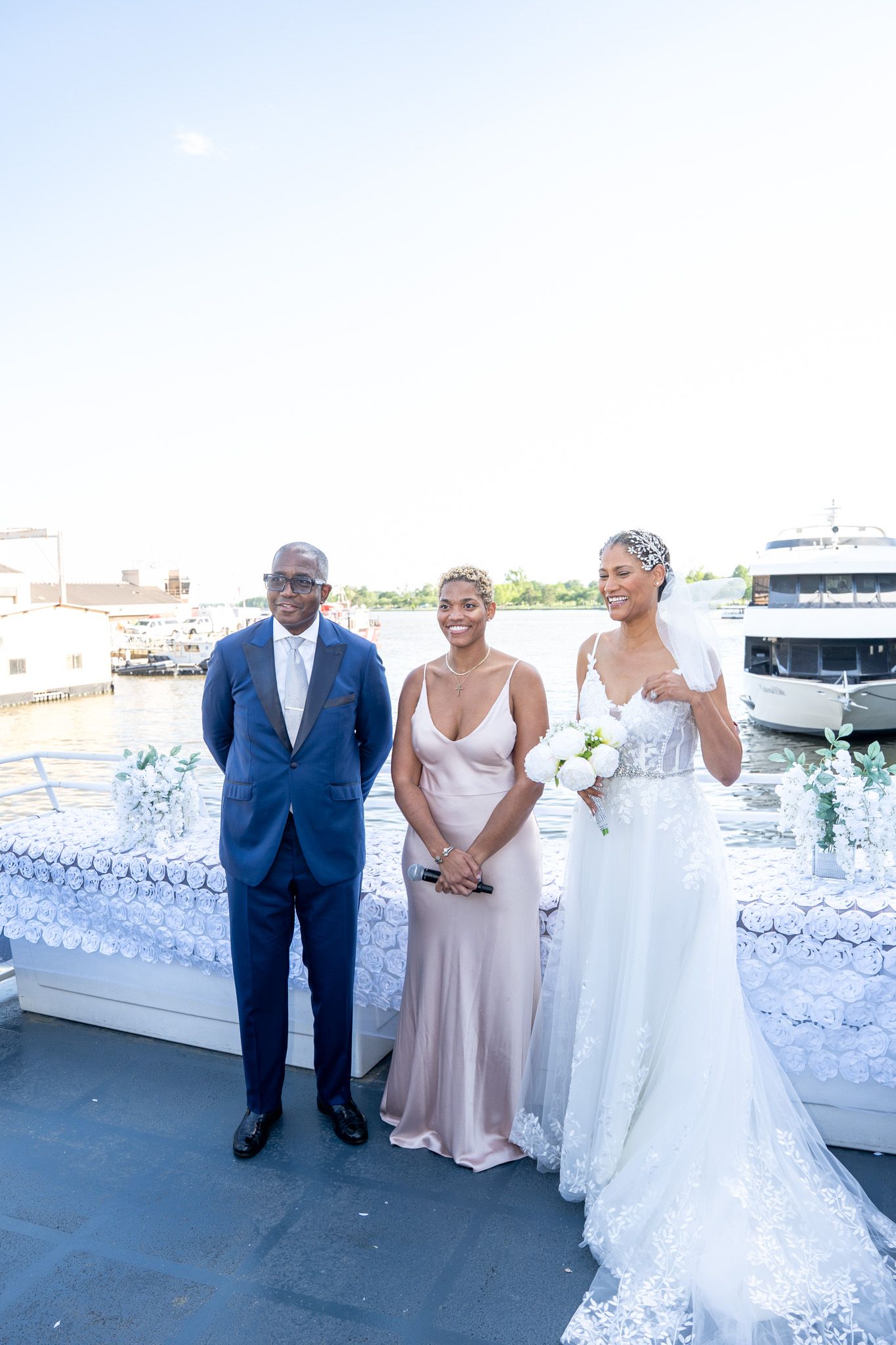 Wedding party members pose together on a boat deck decorated with white floral arrangements.