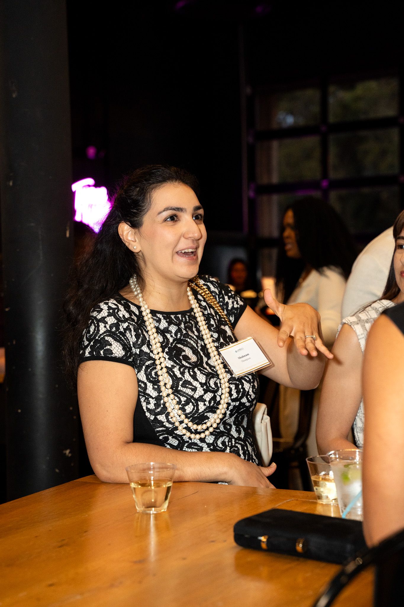 Woman in black and white dress engaged in conversation at social gathering.