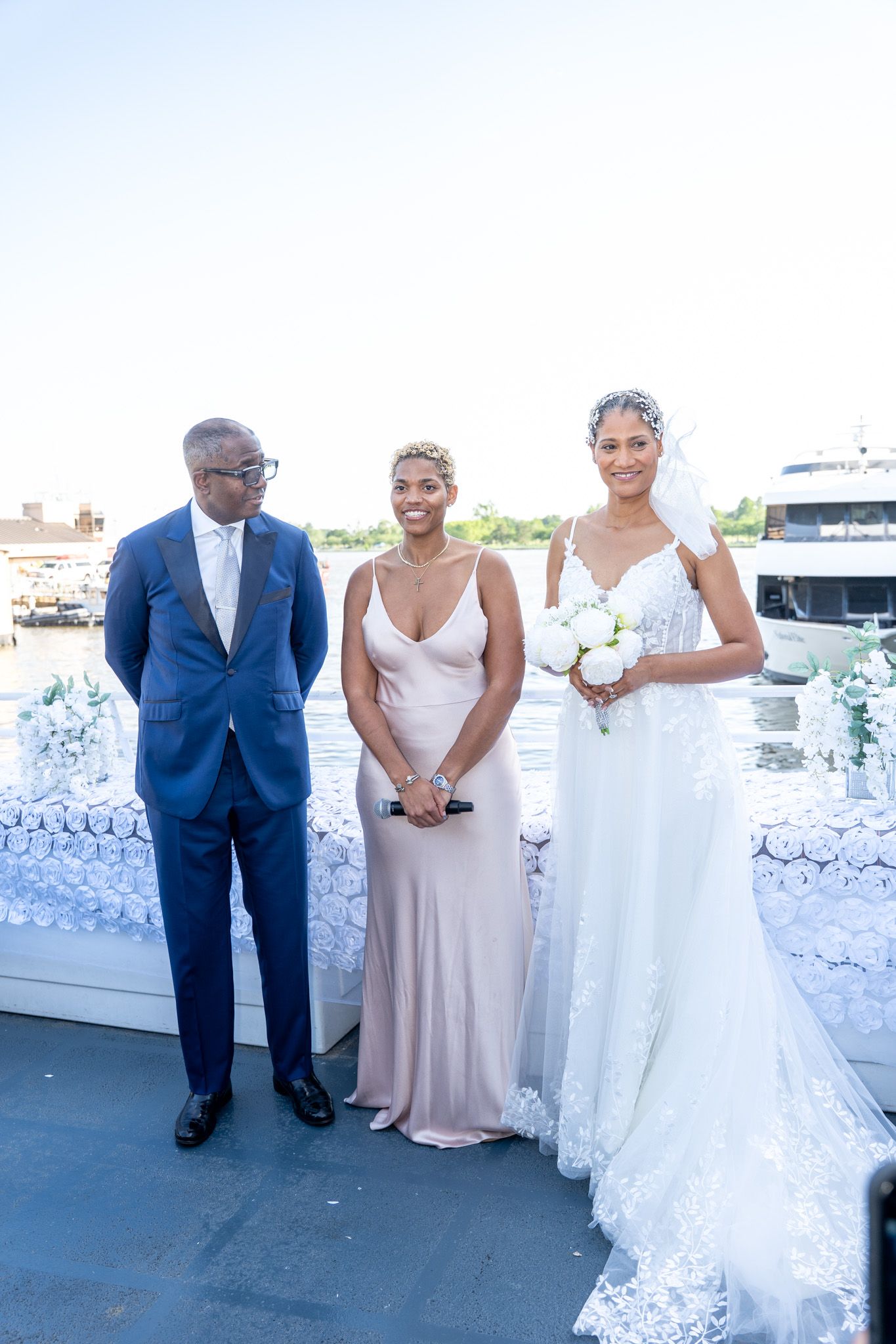 Wedding party members share a lighthearted moment on the dance floor at an elegant reception with white floral decor.