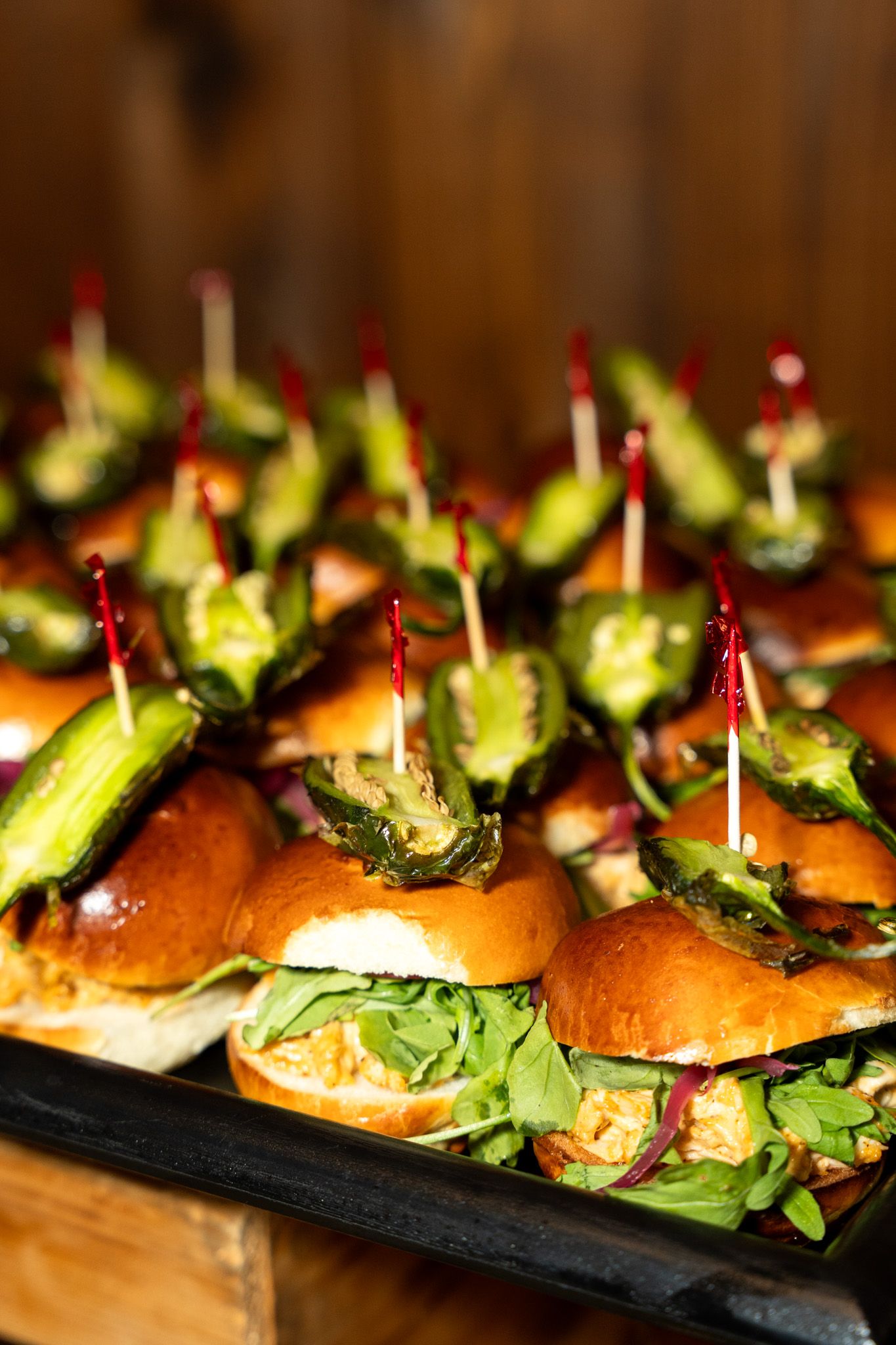 Appetizing mini sliders garnished with fresh greens served on a dark platter.