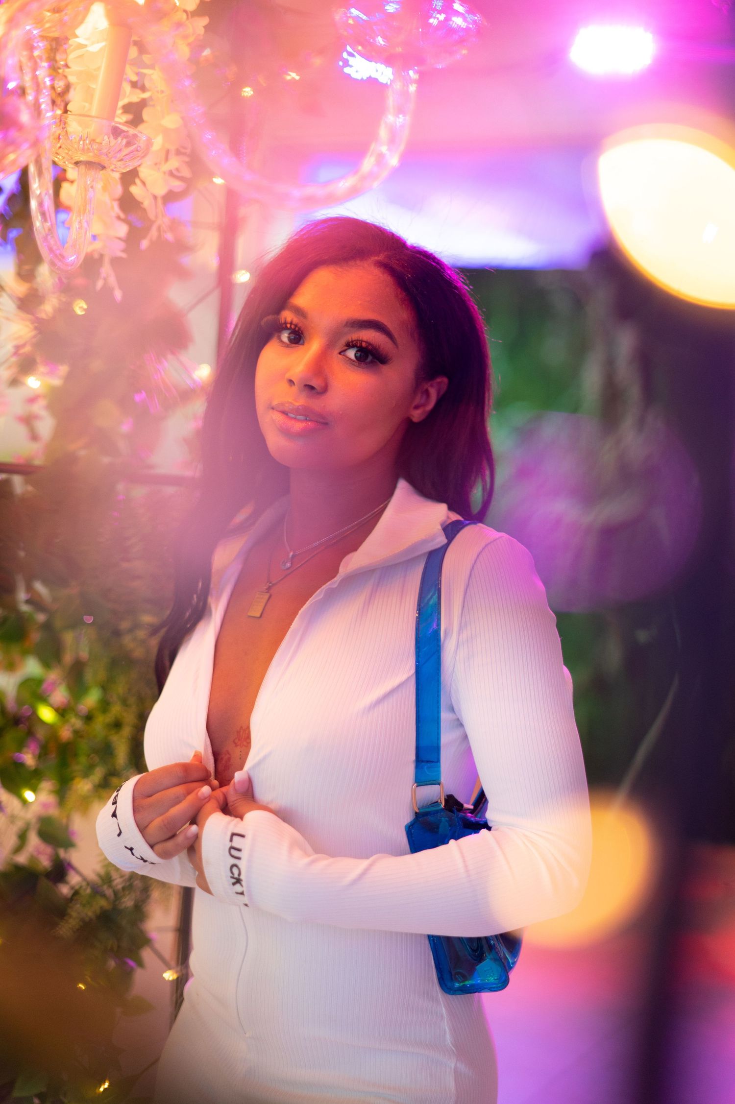 Portrait in white outfit with blue backpack against dreamy pink and purple lighting.