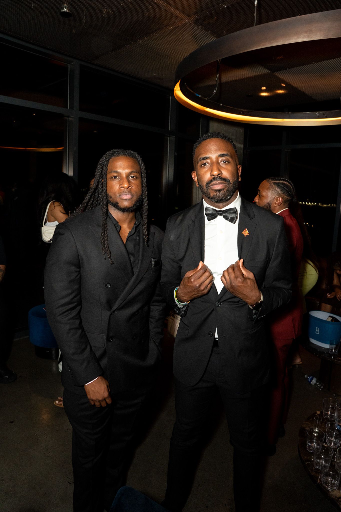 Two people in black suits posing together at an evening event.