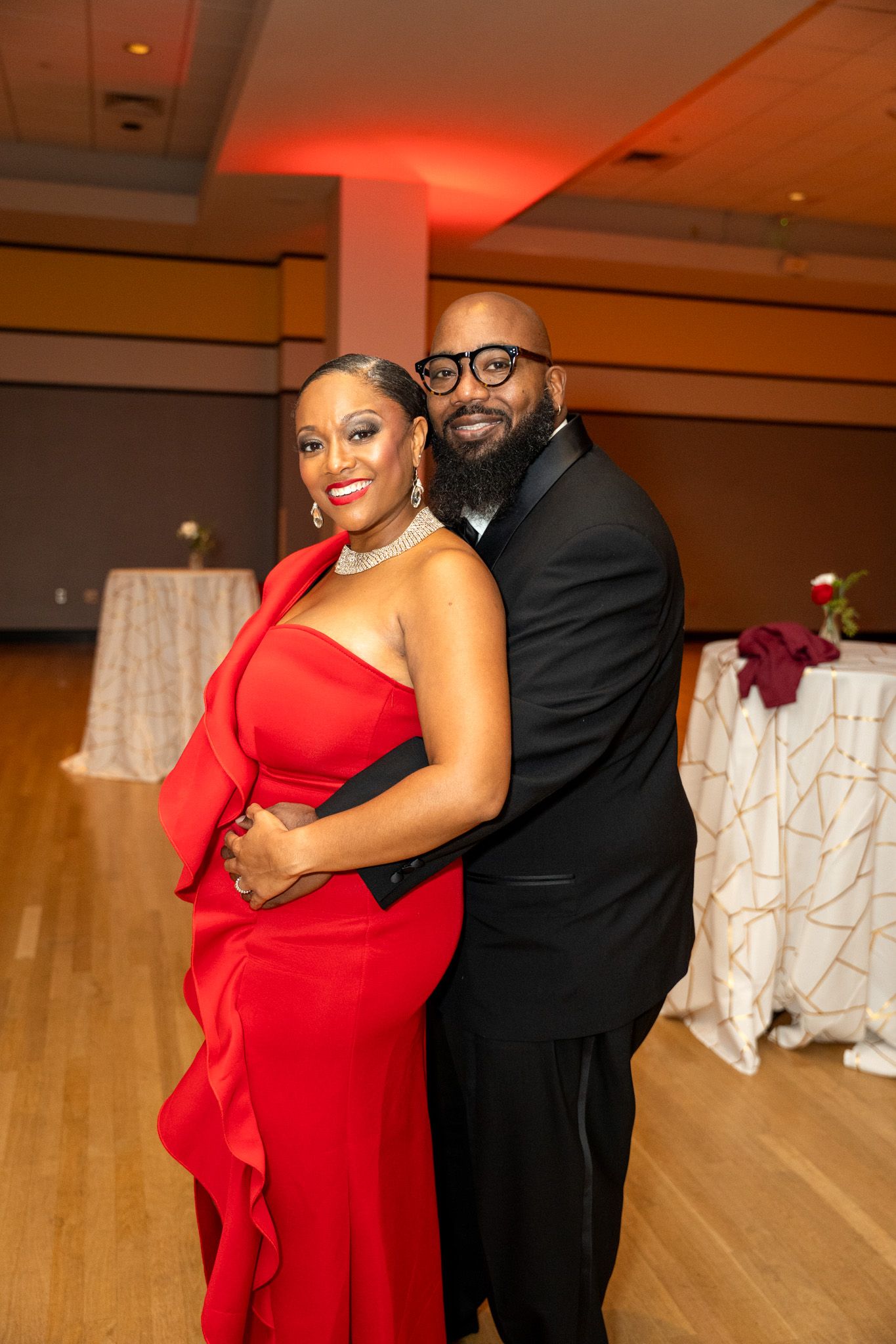 Couple dancing at formal event with red dress and black tie attire.