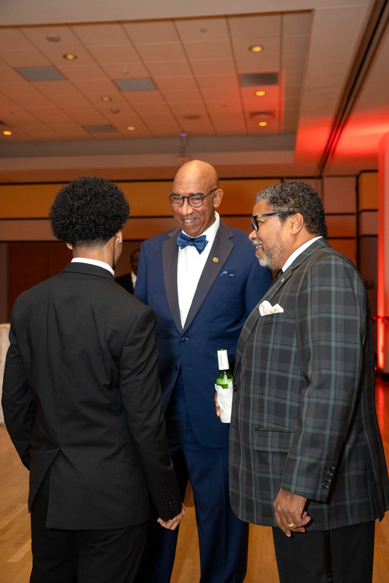 Three guests in formal attire having a conversation at an upscale evening event.