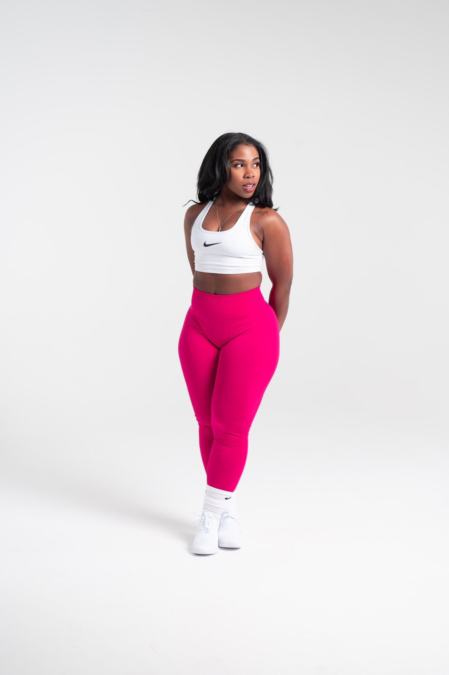 Athletic figure in white sports bra and pink leggings poses against white background.