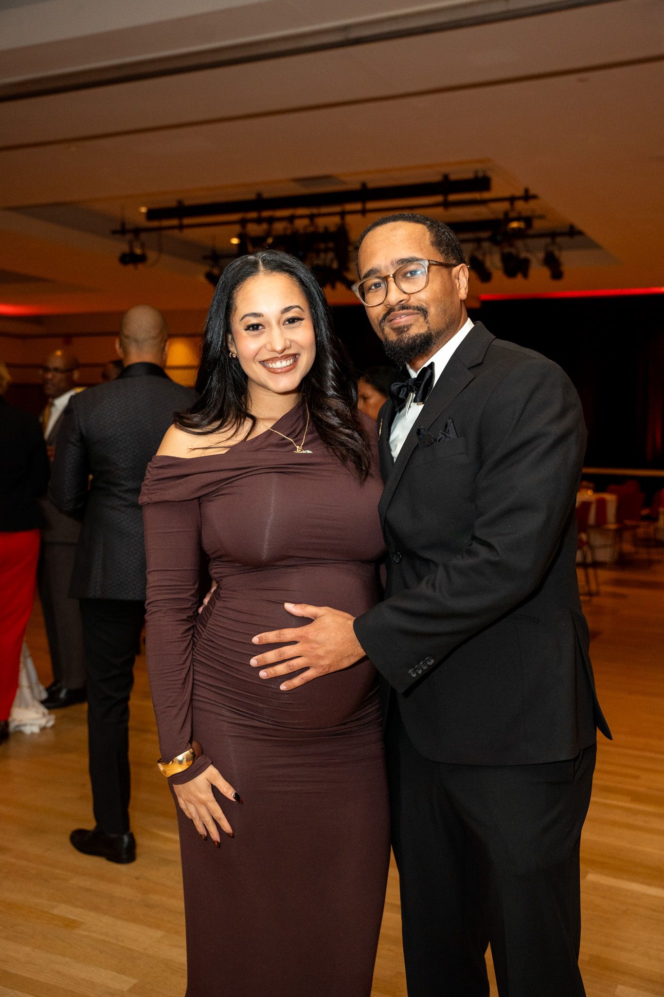 Couple in formal attire posing at an elegant evening event with ambient lighting.