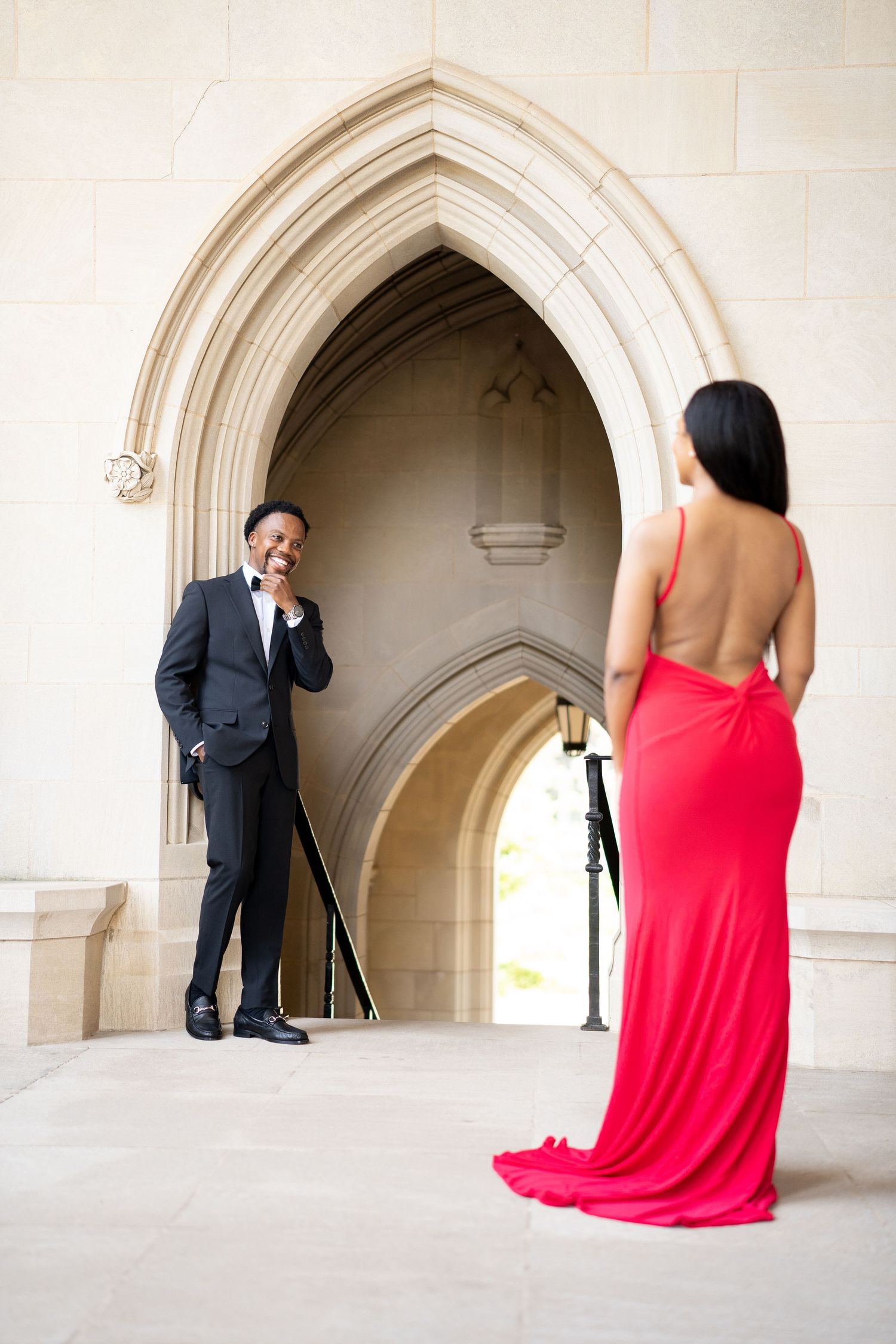 Couple in formal wear shares playful moment under Gothic archway.