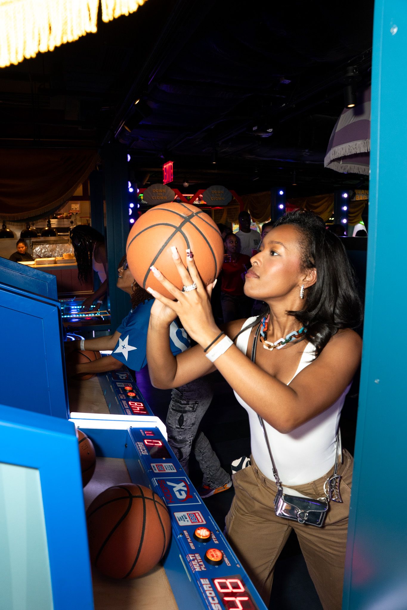 People playing basketball arcade games in a dimly lit entertainment venue.