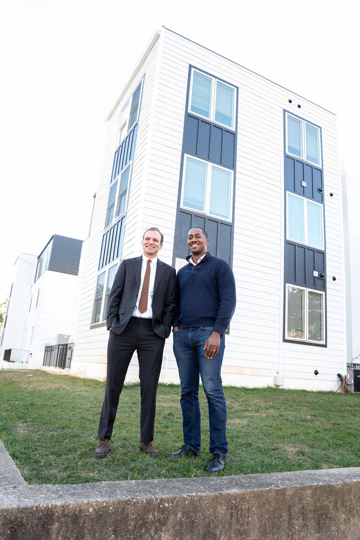 Two professionals stand in front of a white modern building on a grassy area.