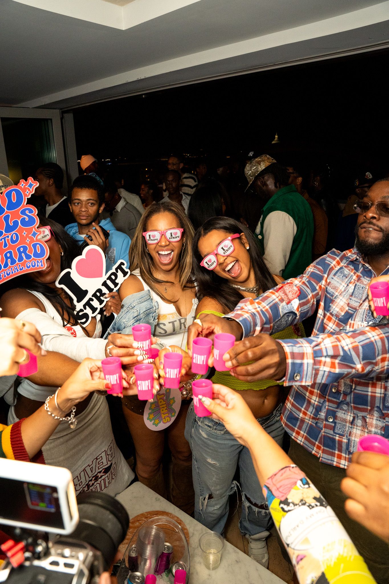 Group of party guests posing with novelty photo props and drinks at a social gathering.