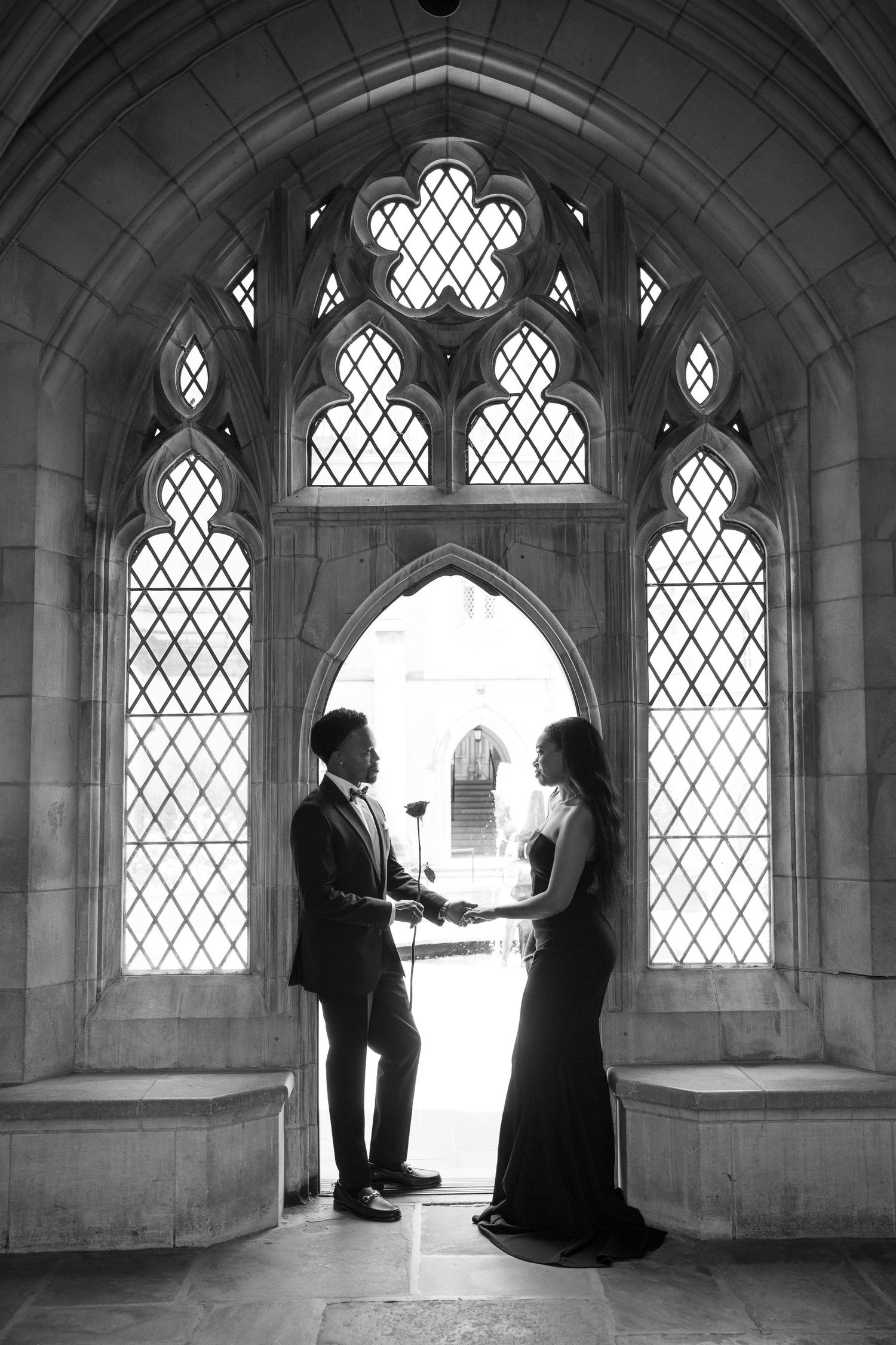 Romantic couple silhouetted against ornate Gothic window with diamond lattice pattern.