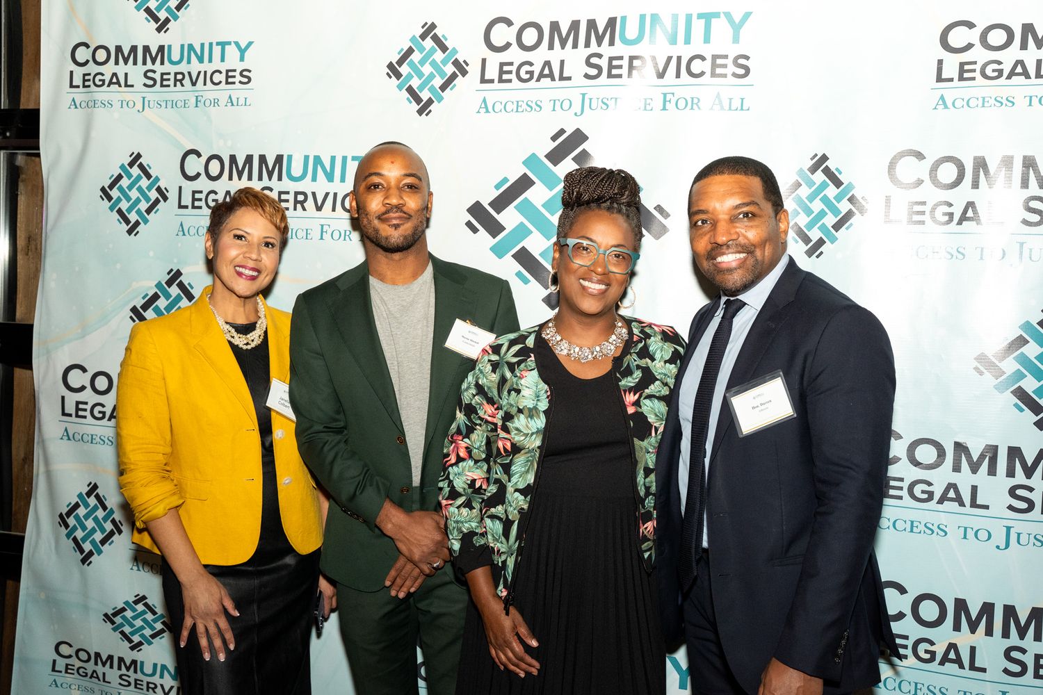 Four professionals pose together at a Community Legal Services event with branded step-and-repeat backdrop.