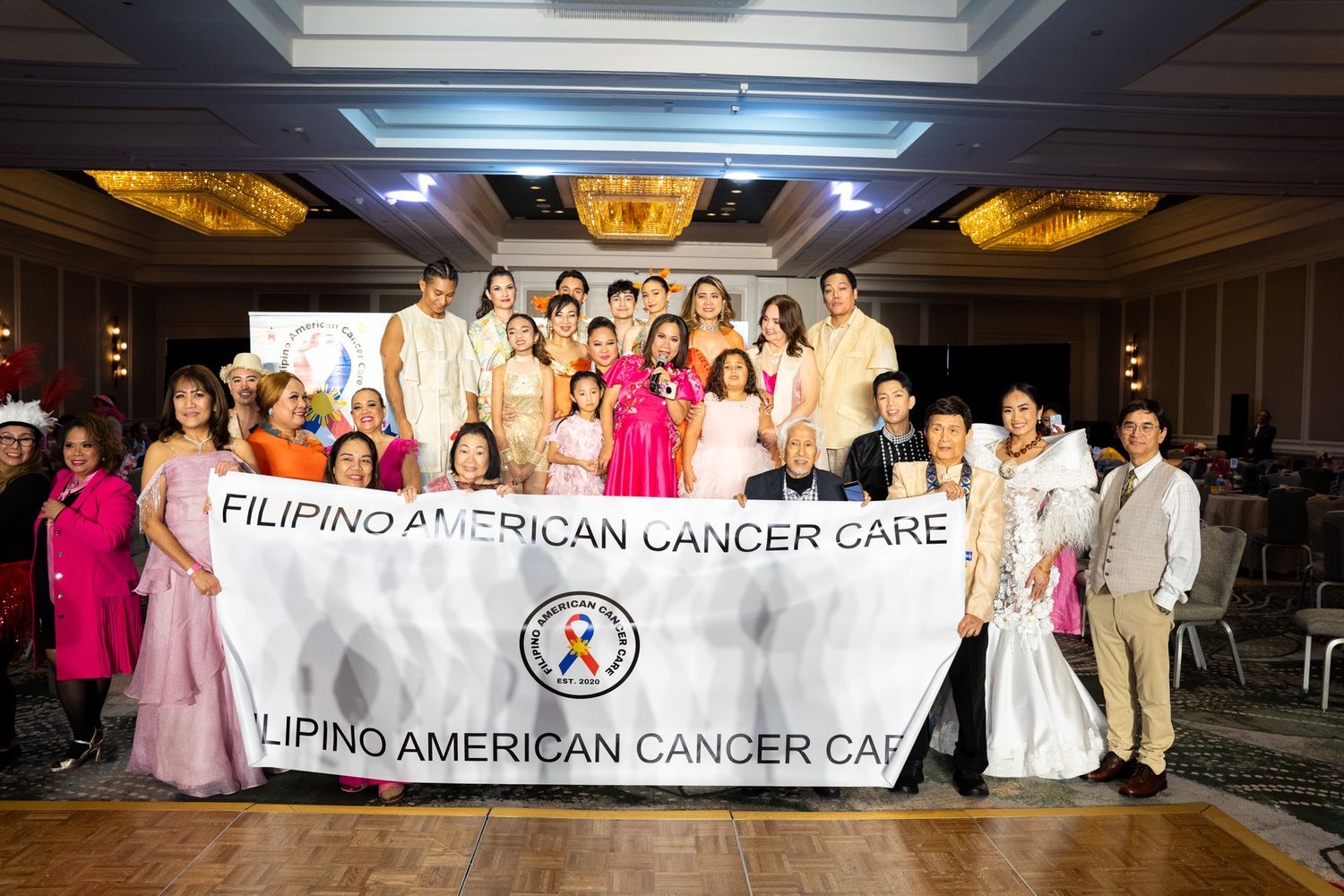 Large group photo of Filipino American Cancer Care organization members holding banners at an indoor event.