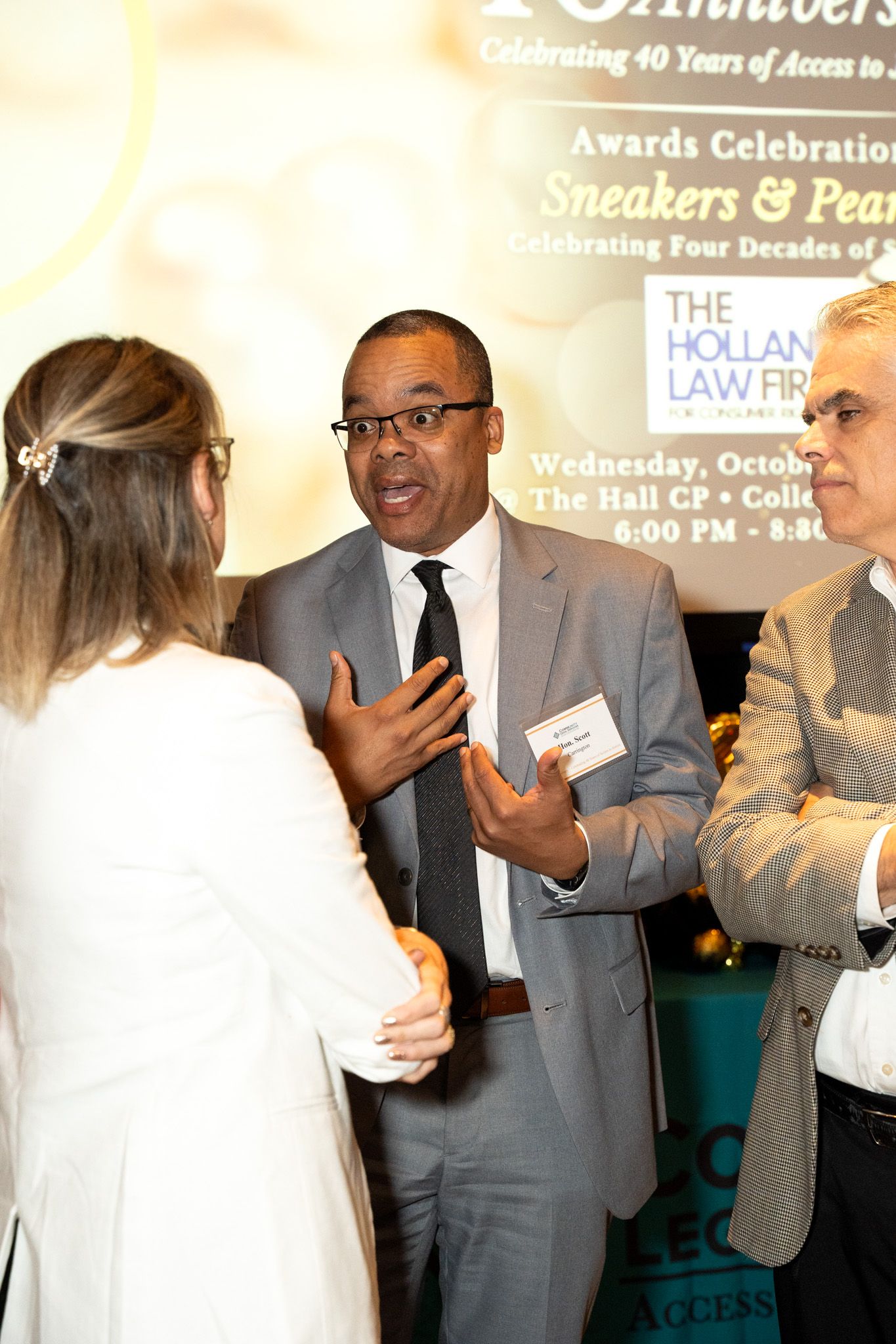 Professional in grey suit gesturing while speaking at networking event.