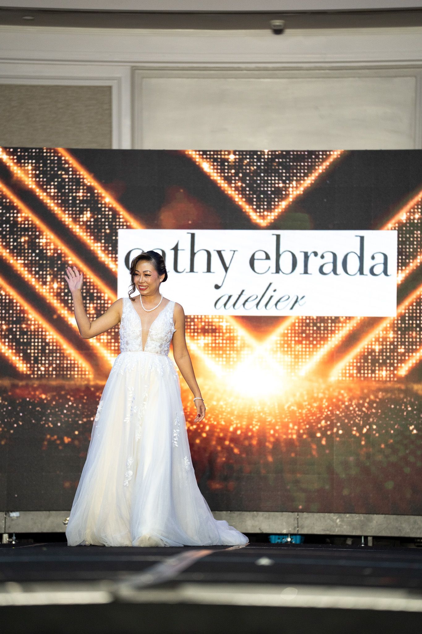 Fashion show runway featuring elegant white wedding gowns against illuminated backdrop.
