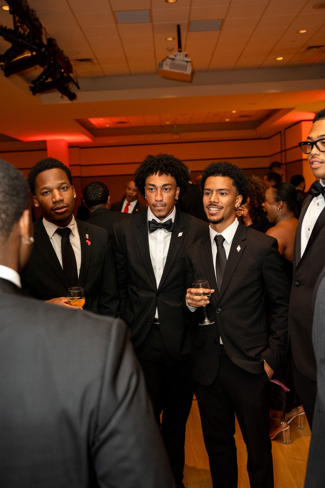 A group in formal black tie attire socializing at an elegant indoor event.