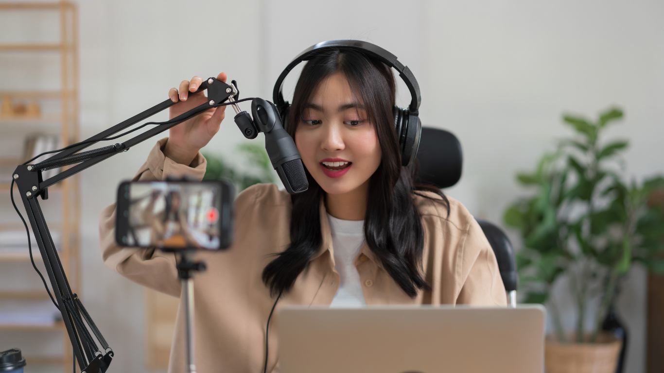 Content creator recording a podcast or video with professional microphone and laptop setup.