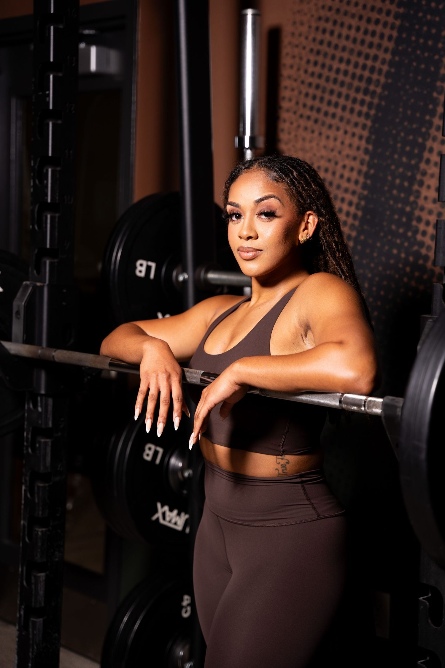 Athletic figure in brown workout gear posing confidently against gym equipment.