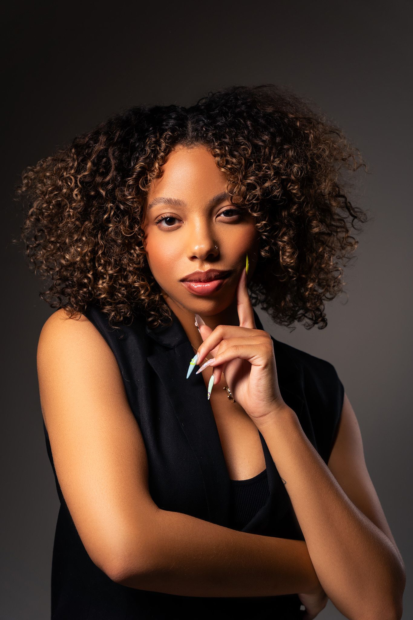 Elegant studio portraits with dramatic lighting showcasing natural curly hair and professional attire.