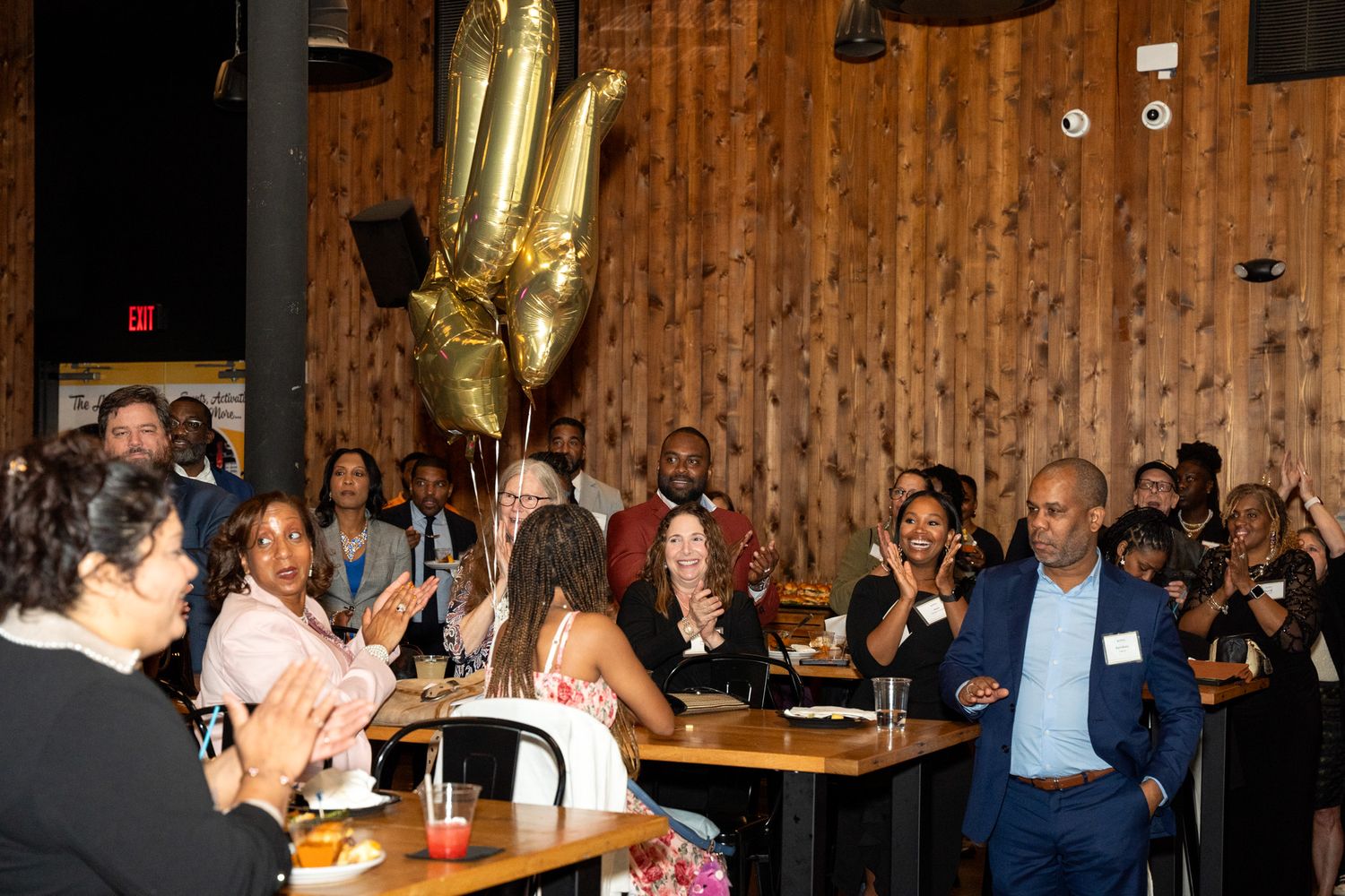 Audience applauding during celebratory event in wood-paneled venue.