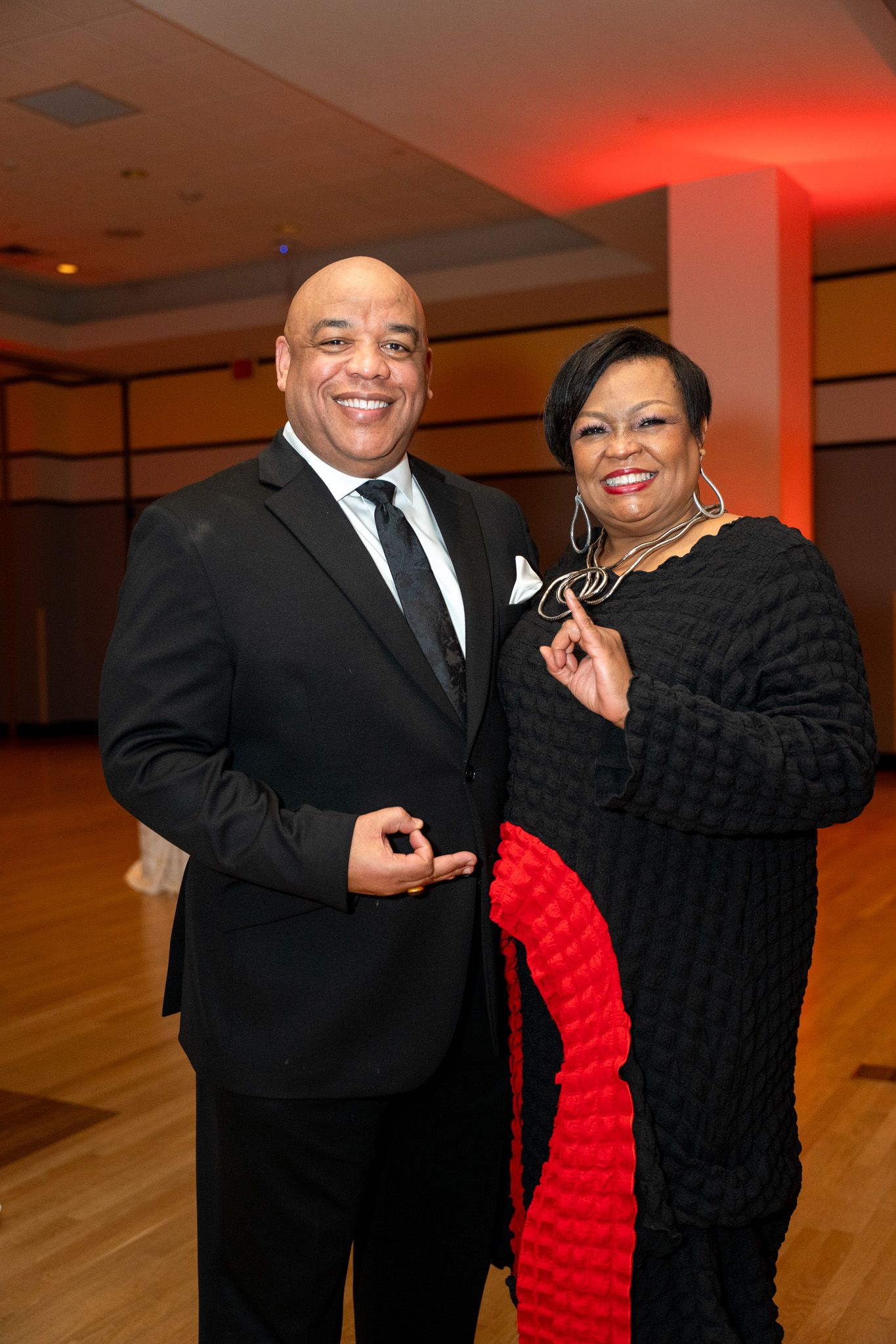 Couple in formal attire dancing at an event with red lighting.