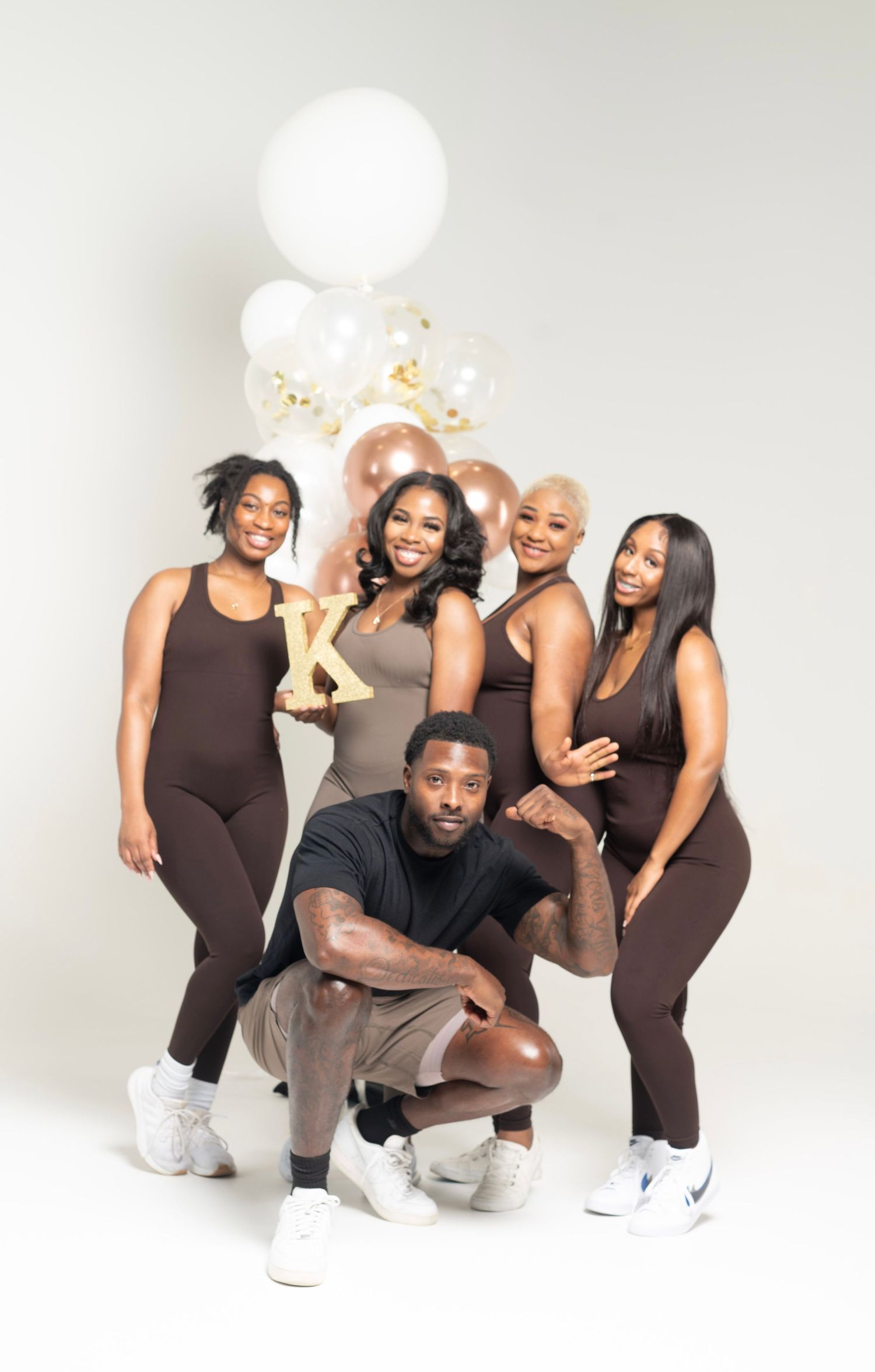 Fitness group photo session with people in black outfits and white balloons against white background.