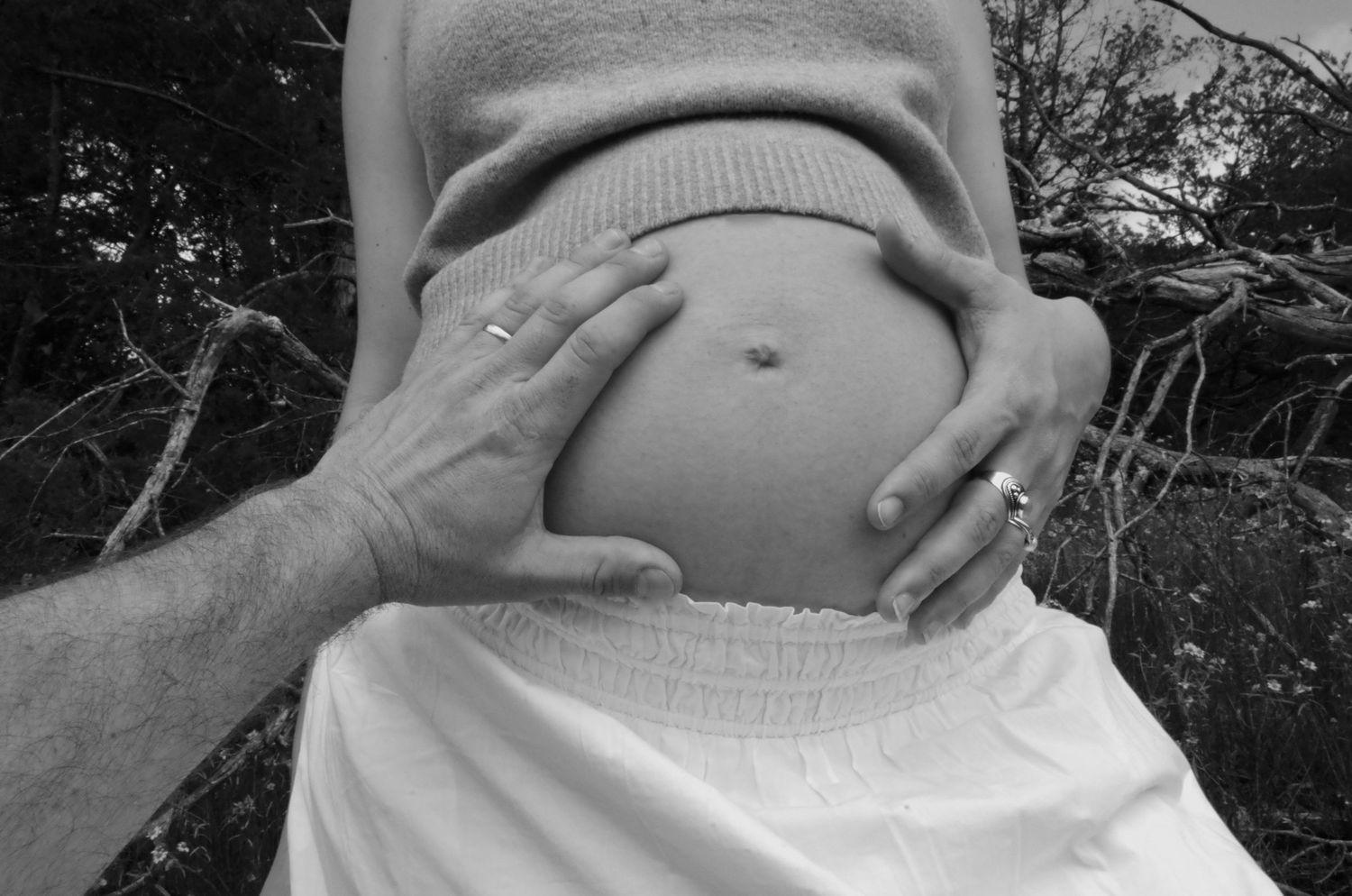 Intimate black and white close-up of a man and woman's hands gently placed on her pregnant belly, symbolizing connection and anticipation.