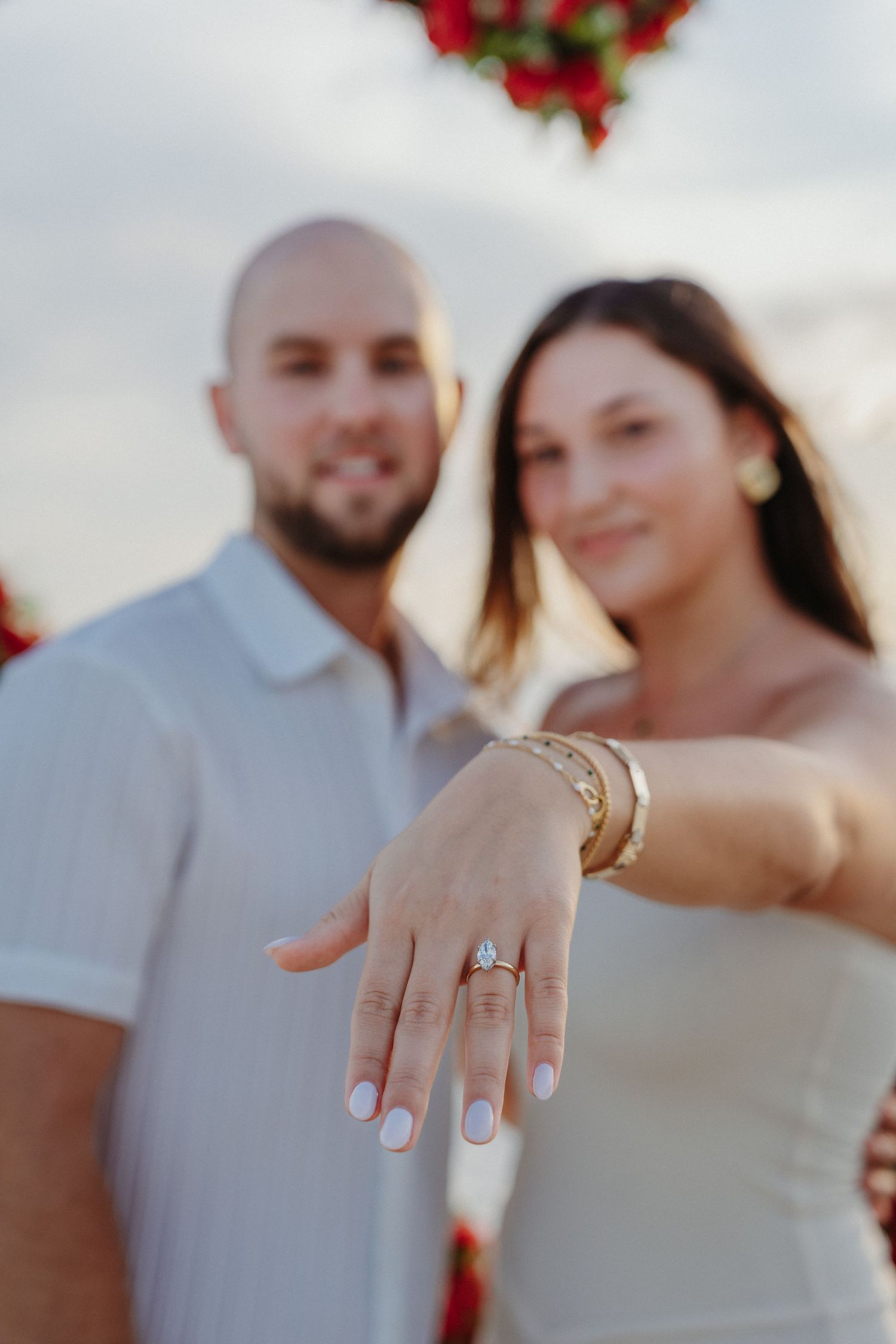 Newly engaged couple displays diamond engagement ring on a beach.