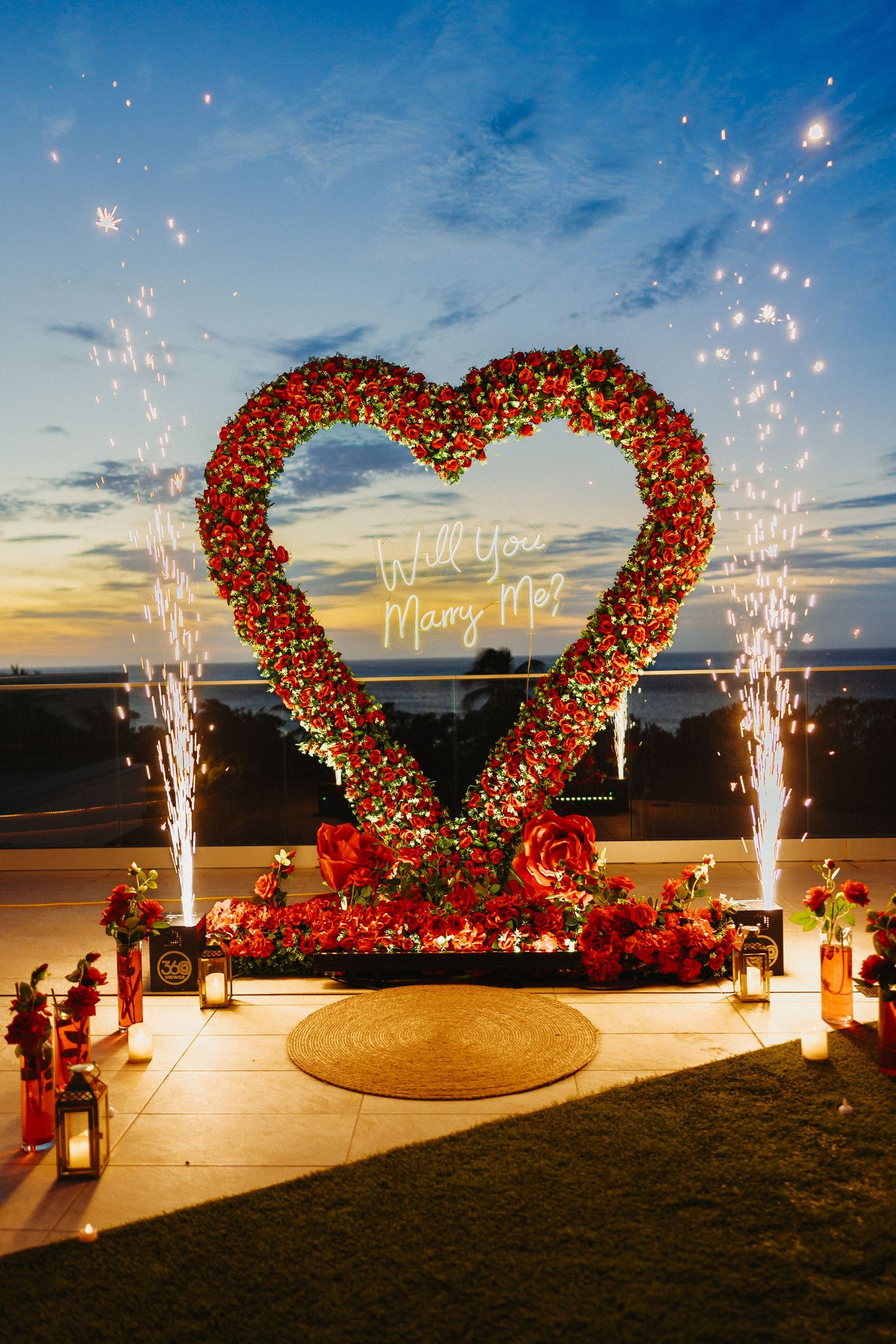 Stunning nighttime marriage proposal setup with floral heart arch, sparklers, and Will You Marry Me neon sign.