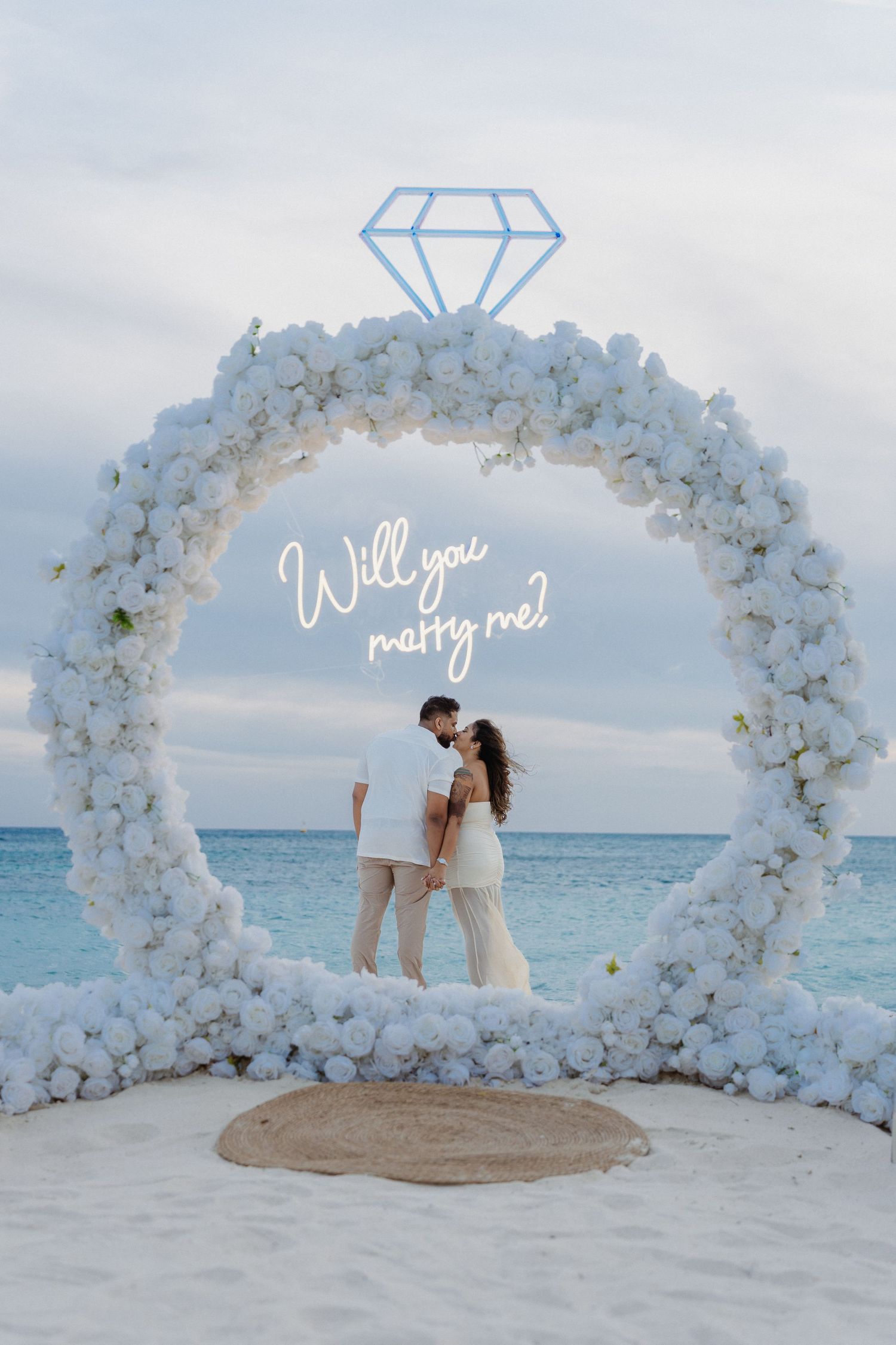 Couple kissing inside a circular white flower arch with a glowing diamond ring and 