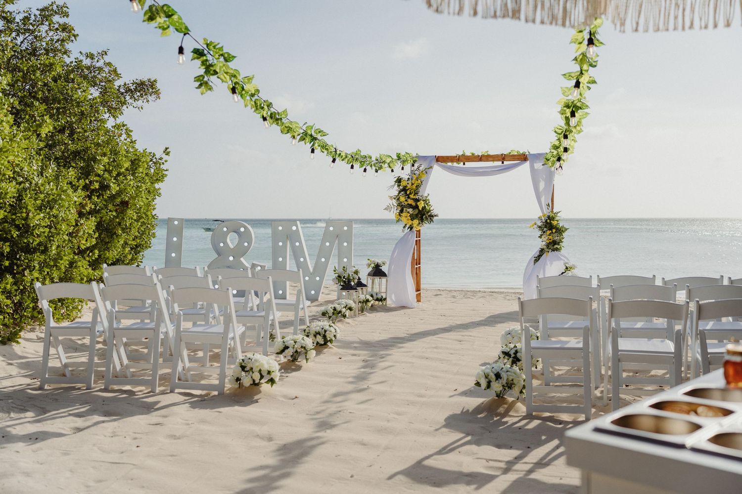Elegant beach wedding setup with white chairs, floral arch, and monogram letters by the ocean.
