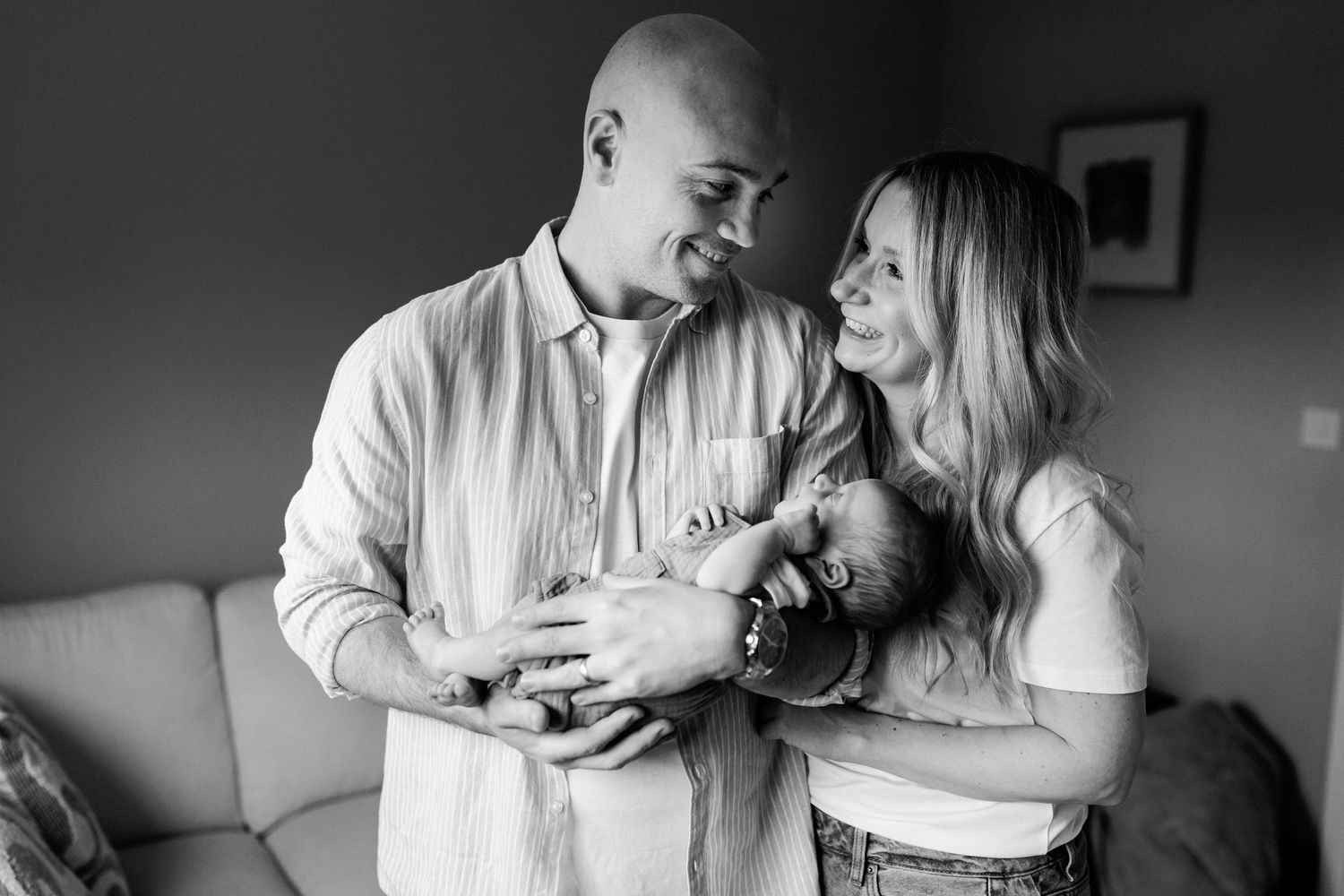 Happy parents smiling and holding their newborn baby together in black and white family portrait photo.