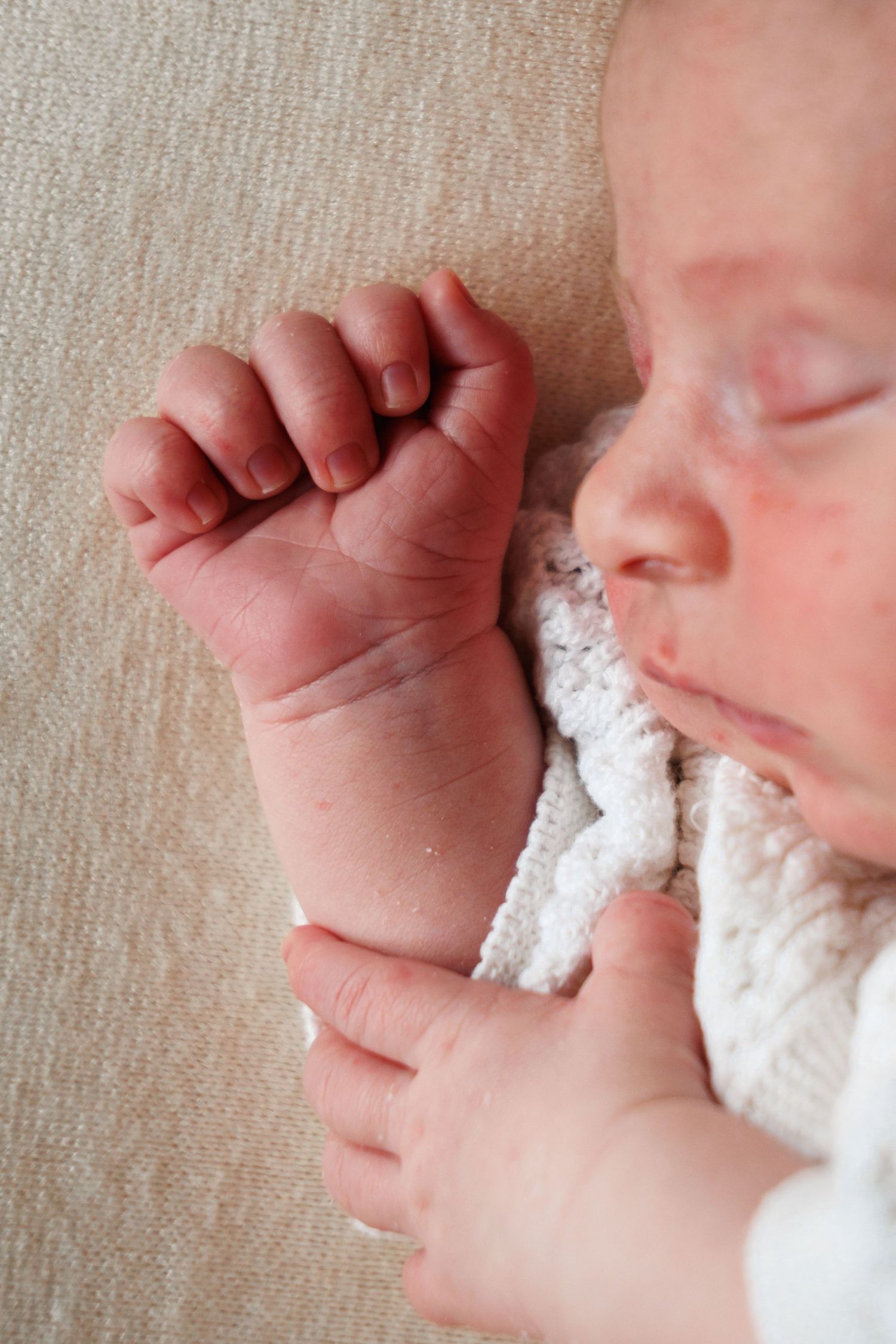 Sleeping newborn baby with tiny clenched fist resting on white knit blanket.